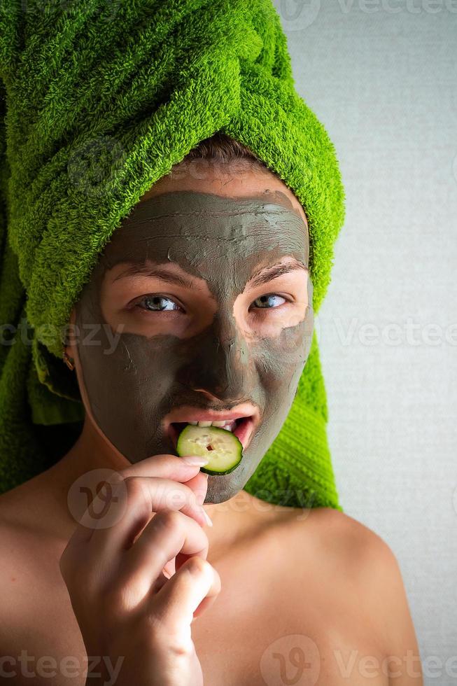 schöne junge frau mit gesichtsmaske auf ihrem gesicht, die gurkenscheiben hält. foto