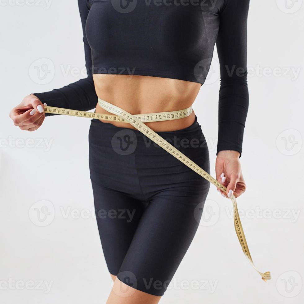 Nahaufnahme der sportlichen Frau mit Maßband im Studio vor weißem Hintergrund foto