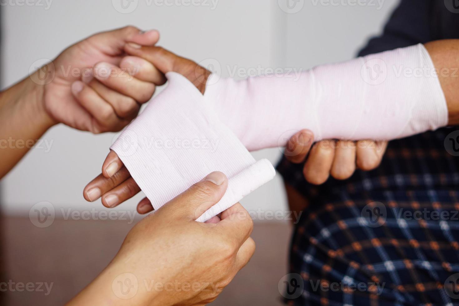 Die Hände des Nahaufnahmemanns wickeln das verstauchte Handgelenk des Patienten mit einem elastischen Verband ein. konzept, erste hilfe und behandlung von armverletzungen . Unfall. Versicherung. foto