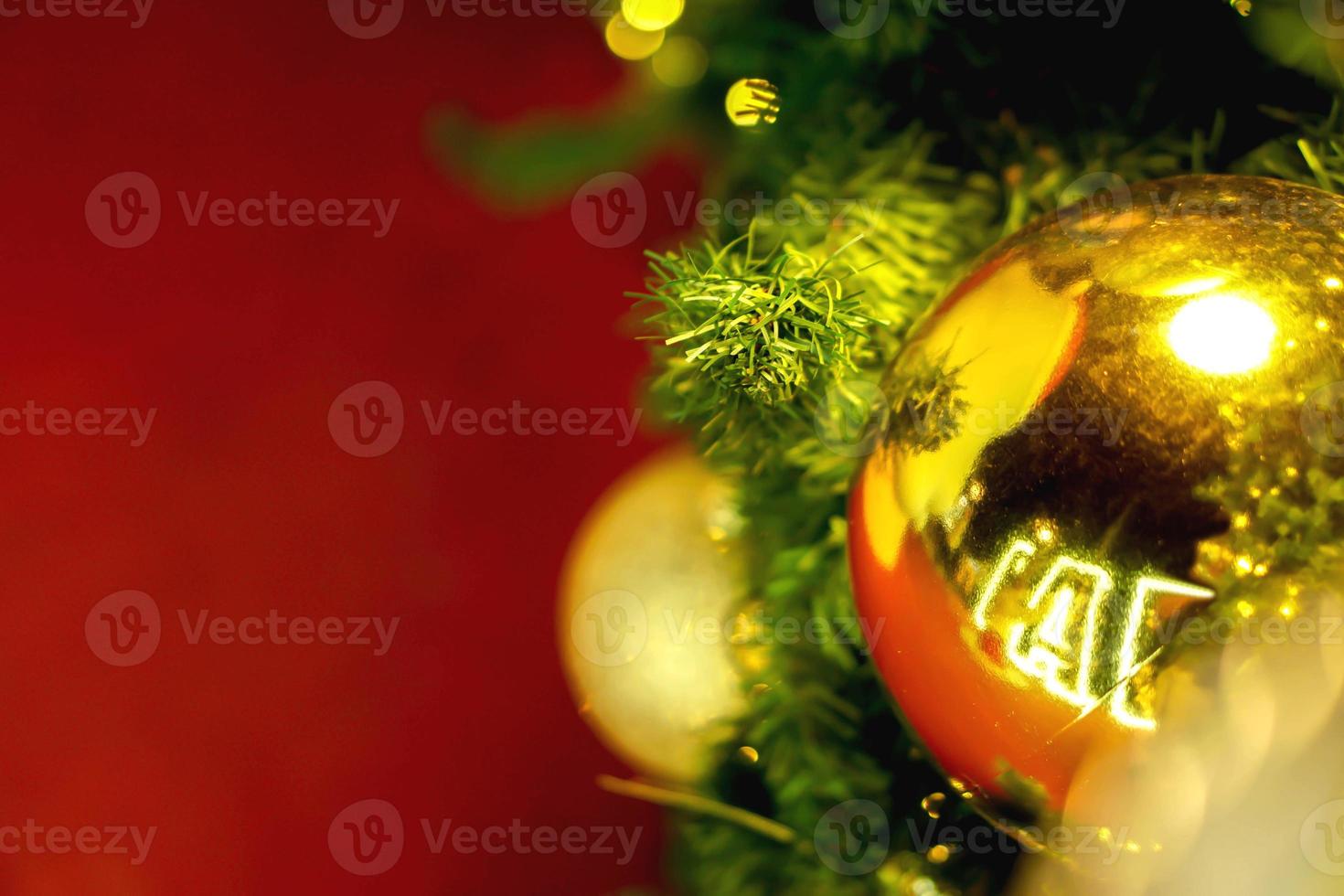 goldene weihnachtskugeln der nahaufnahme verziert auf kiefer am weihnachtstag und rotem hintergrund foto