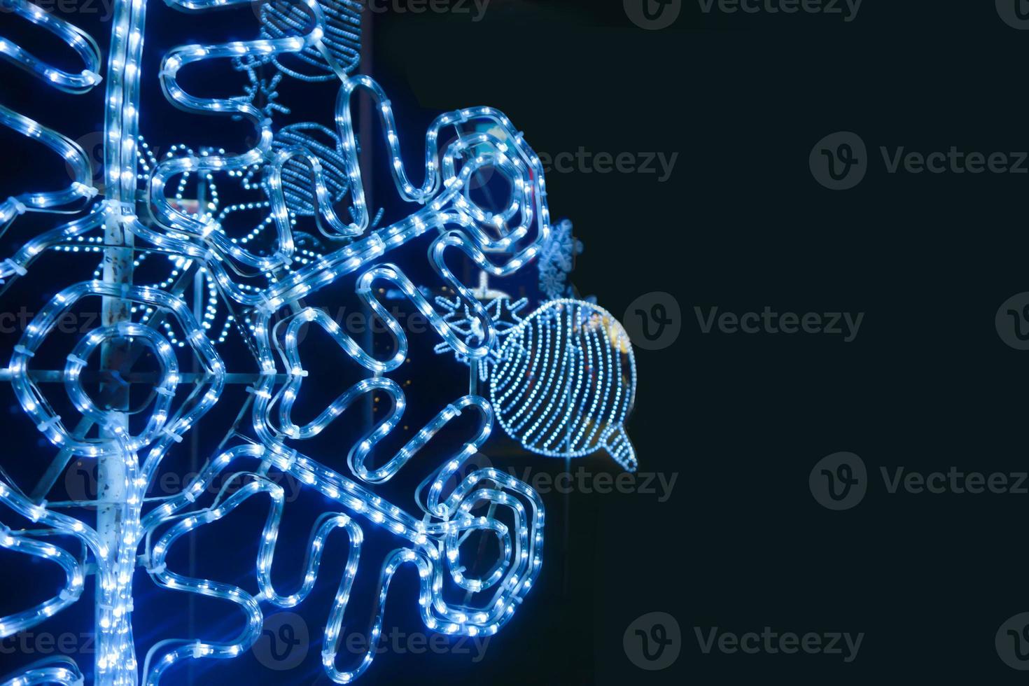 Nahaufnahme und Ernte verzierte LED von weihnachtlicher blauer Beleuchtung in Schneeflockenform isolieren auf schwarzem Hintergrund. foto