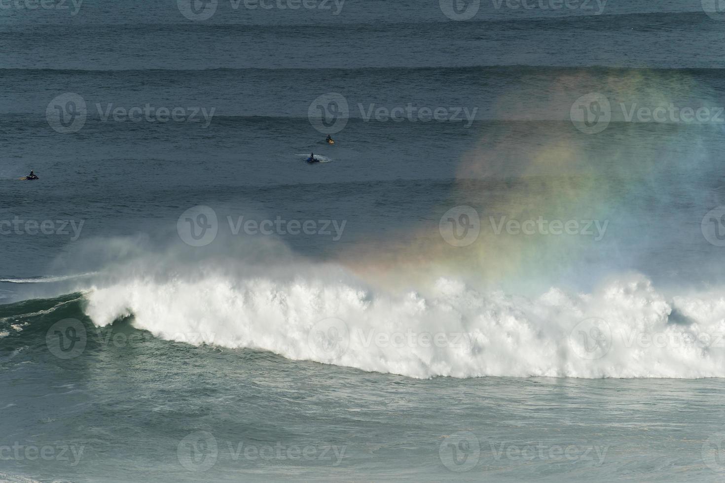 große riesige wellen, die in nazare, portugal, zusammenbrechen und einen regenbogen im ozean schaffen. Surfer und Jetskis im Wasser. größten wellen der welt. touristisches Ziel zum Surfen. foto