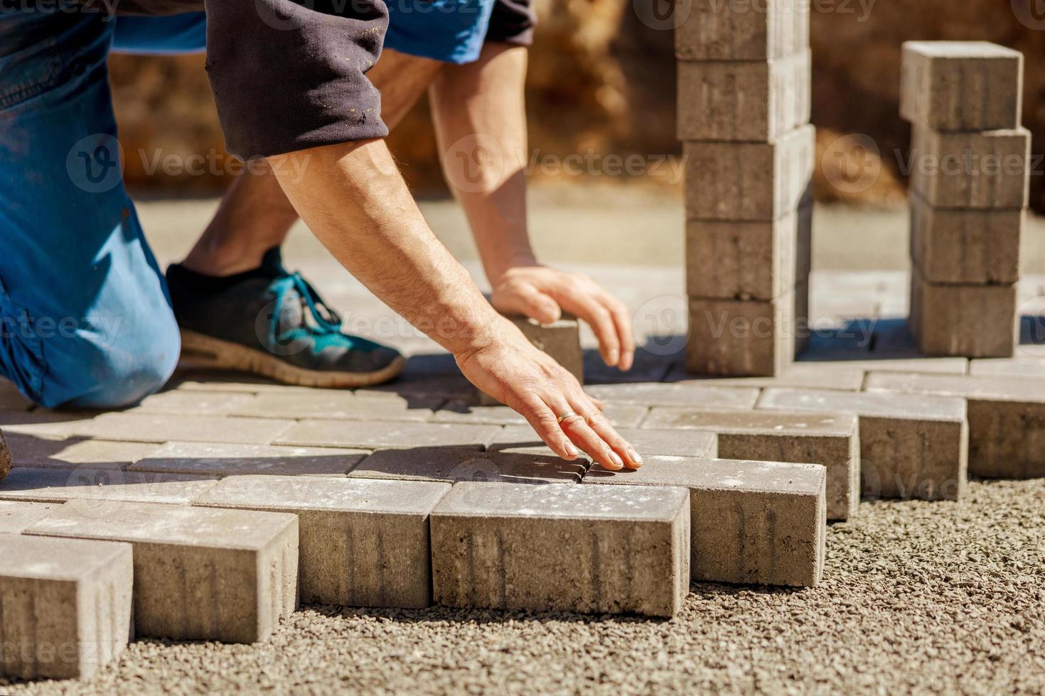 Junger Mann, der graue Betonplatten im Innenhof des Hauses auf Kiesfundament legt. Meister legt Pflastersteine. Pflasterung des Gartenziegelwegs durch einen professionellen Straßenfertiger. Bürgersteig reparieren. foto