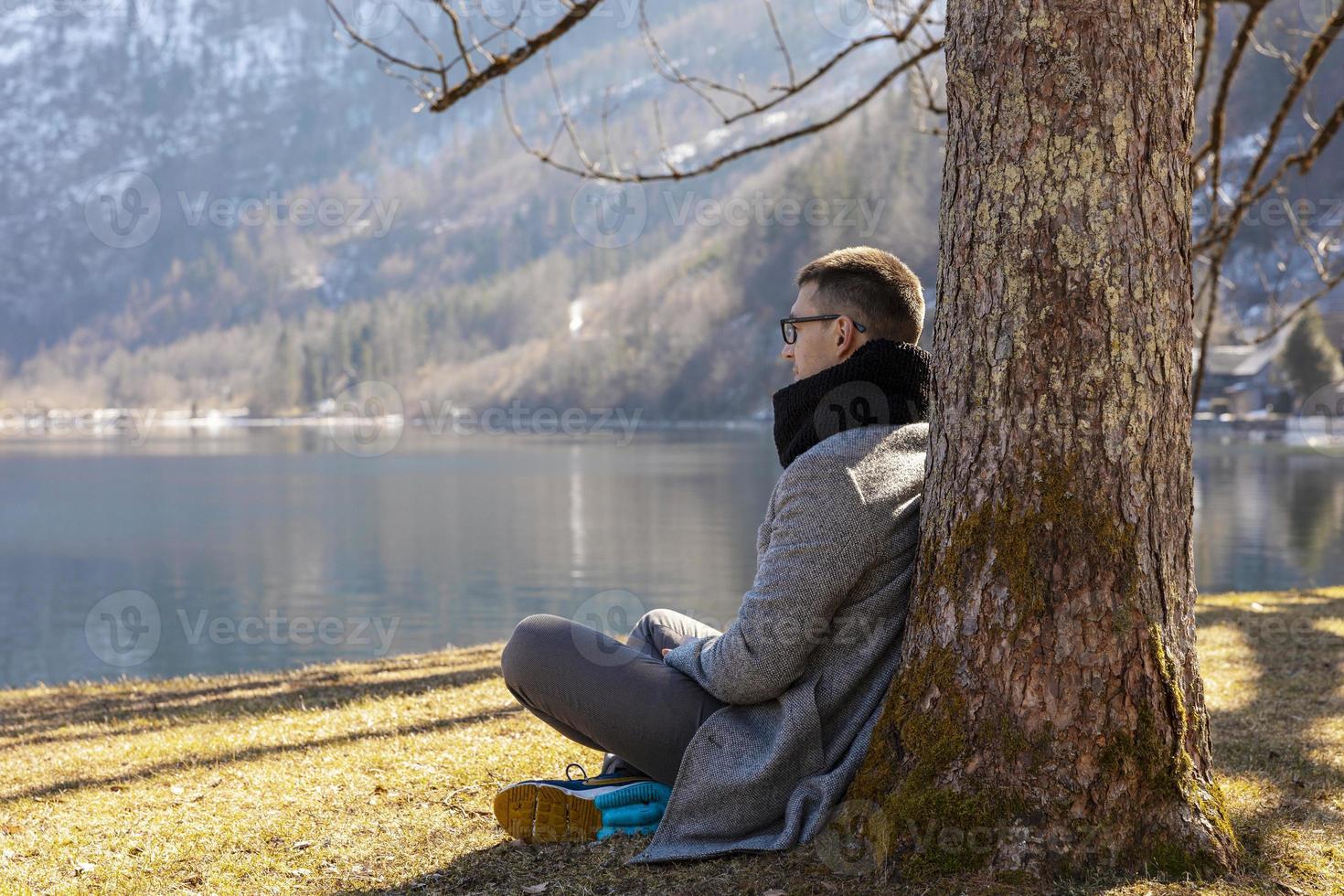 junger mann, der draußen sitzt und berge, schnee, see, gutes wetter, blauer himmel, sonne genießt. schöne Landschaft. Zeit mit sich selbst, Träumen, Entspannung, mentale Gesundheit. Tourismus, Urlaub und Reisen. foto