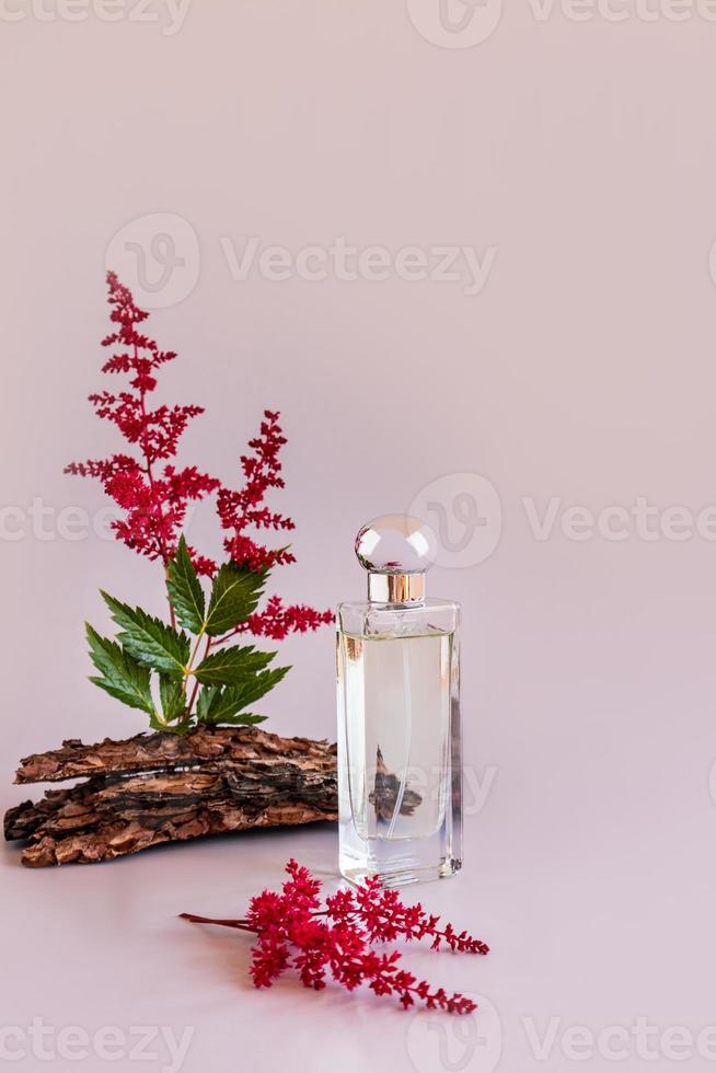 Eine Flasche Parfüm oder Toilettenwasser für Frauen auf einem rosafarbenen Hintergrund mit Blumen und Baumrinde. Präsentation des Aromas eines natürlichen Geruchs. foto