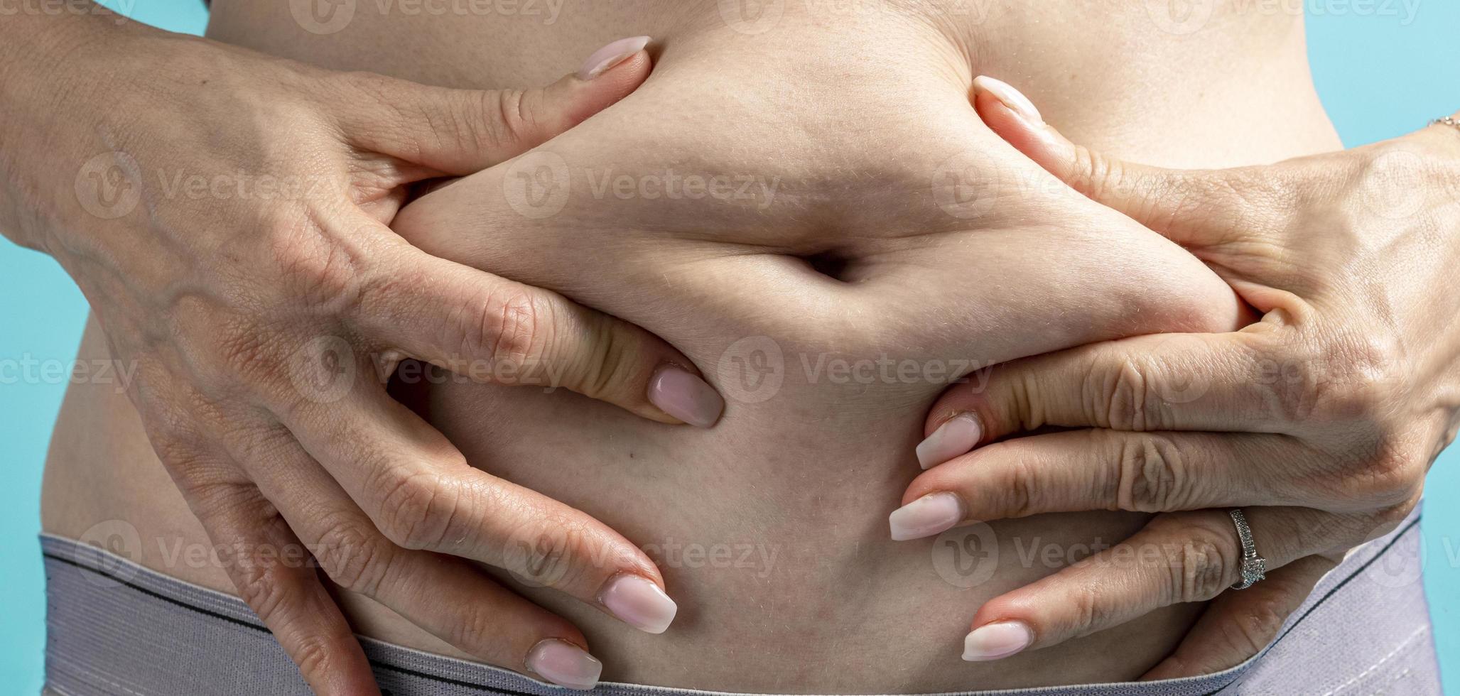 Frau mit dickem Bauch, die eine fette Rolle auf ihrem Bauch auf blauem Hintergrund drückt. foto