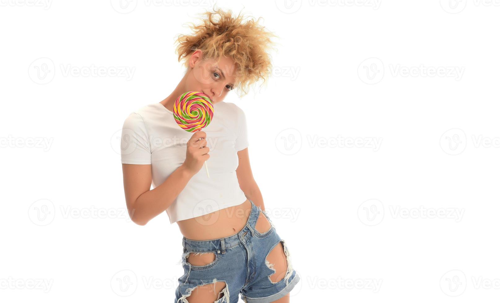 blonde Frau, die süße Süßigkeiten leckt. weibliches Modell, das köstlichen Süßwarenlutscher mit überraschtem Ausdruck isst. Studioaufnahme isolierter weißer Hintergrund, foto