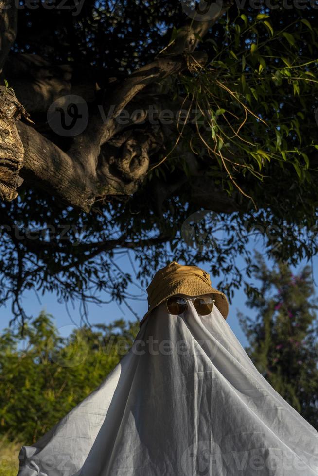 Halloween feiern. geisterherausforderung 2021. ein mann, der als geist aus einem blatt und einer sonnenbrille verkleidet ist, überquert die straße entlang des zebrastreifens. gruselige Jahreszeit. foto