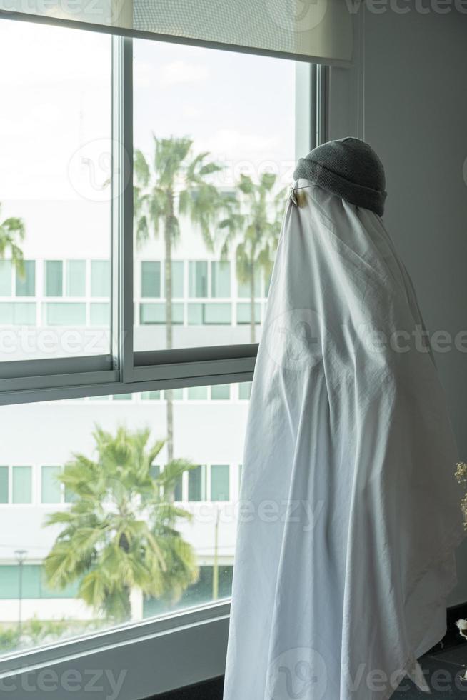 Halloween feiern. geisterherausforderung 2021. ein mann, der als geist aus einem blatt und einer sonnenbrille verkleidet ist, überquert die straße entlang des zebrastreifens. gruselige Jahreszeit. foto