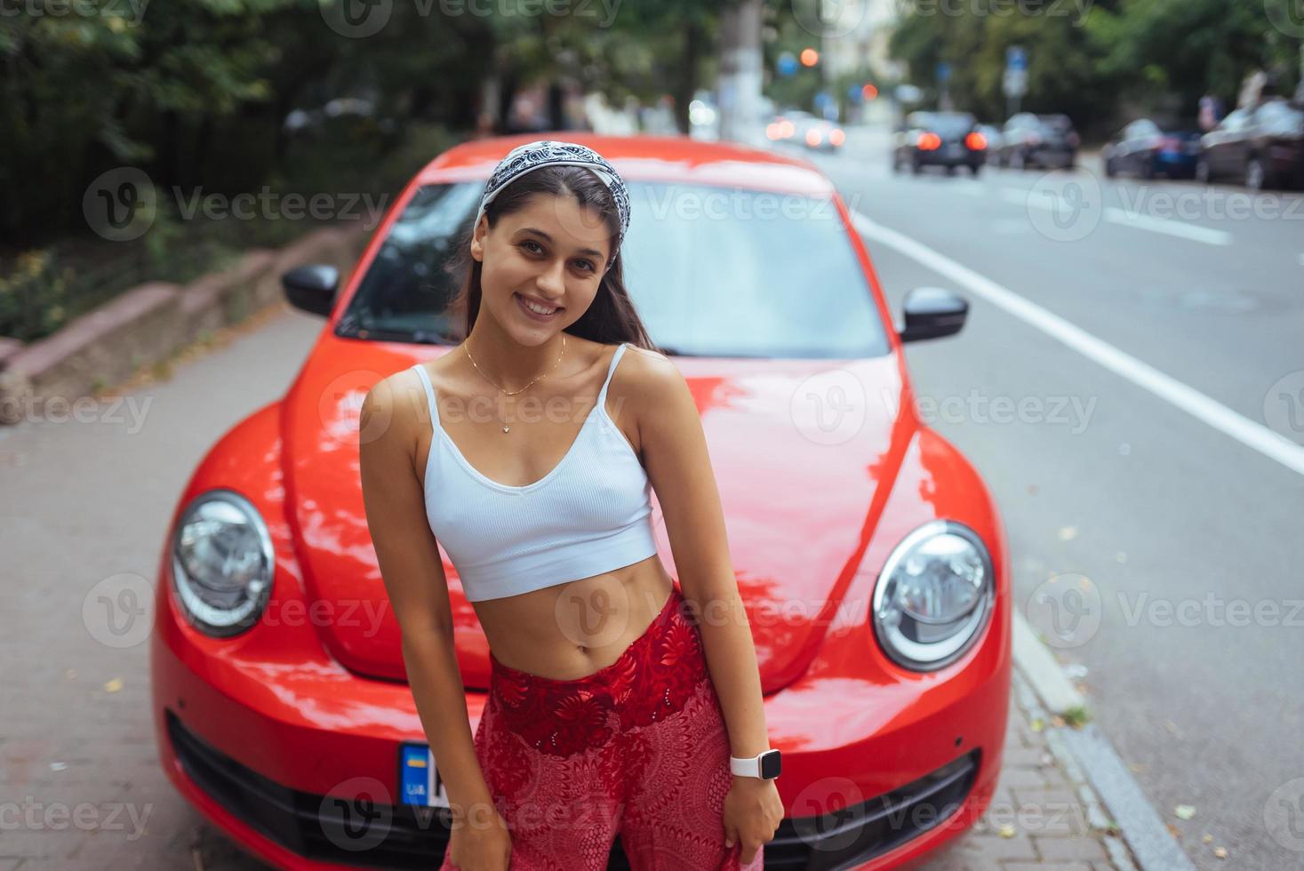 Porträt einer hübschen kaukasischen Frau, die gegen ein neues rotes Auto steht foto