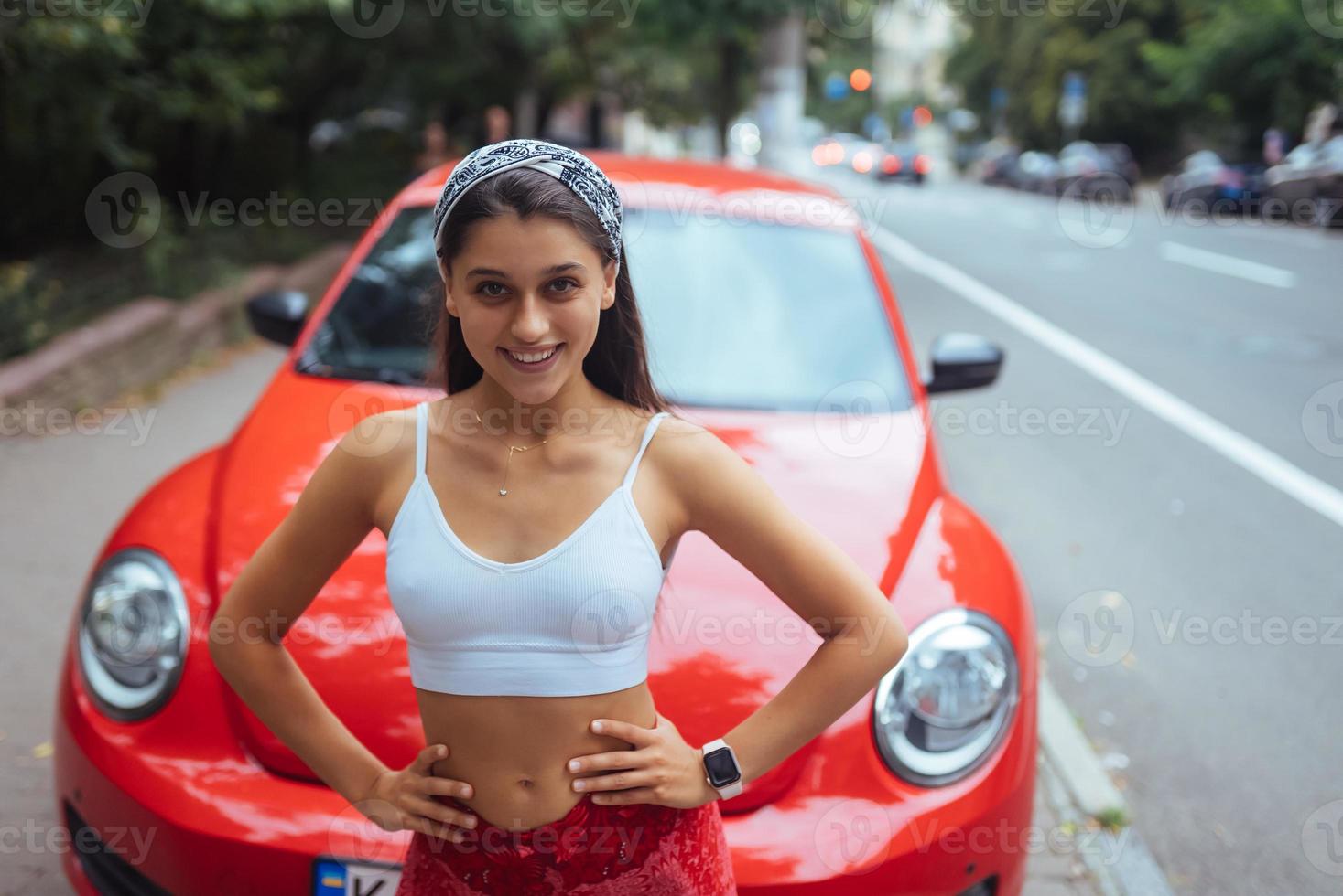 Porträt einer hübschen kaukasischen Frau, die gegen ein neues rotes Auto steht foto