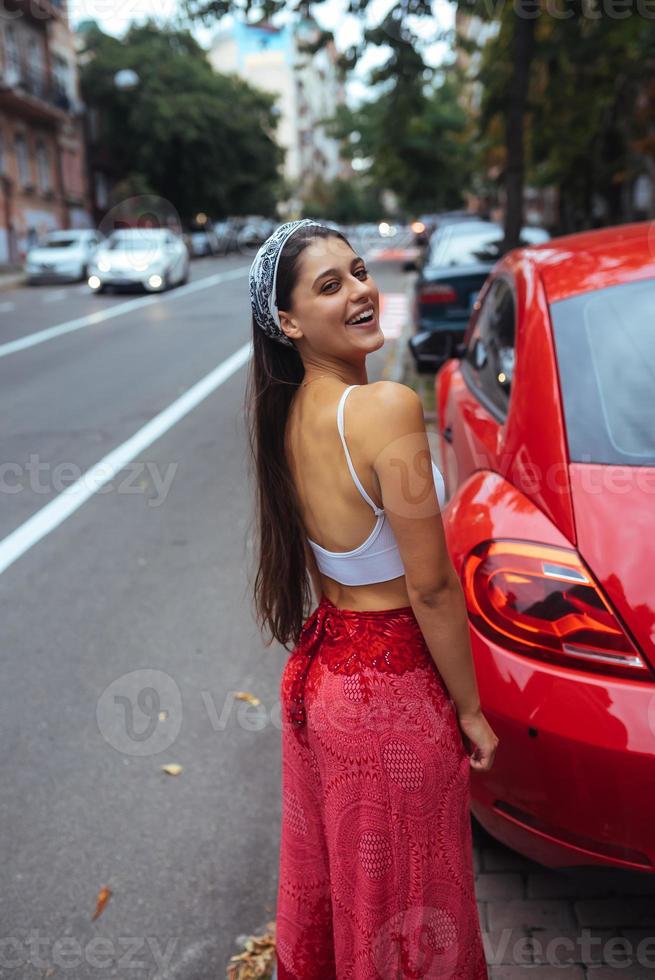 Porträt einer hübschen kaukasischen Frau, die gegen ein neues rotes Auto steht foto