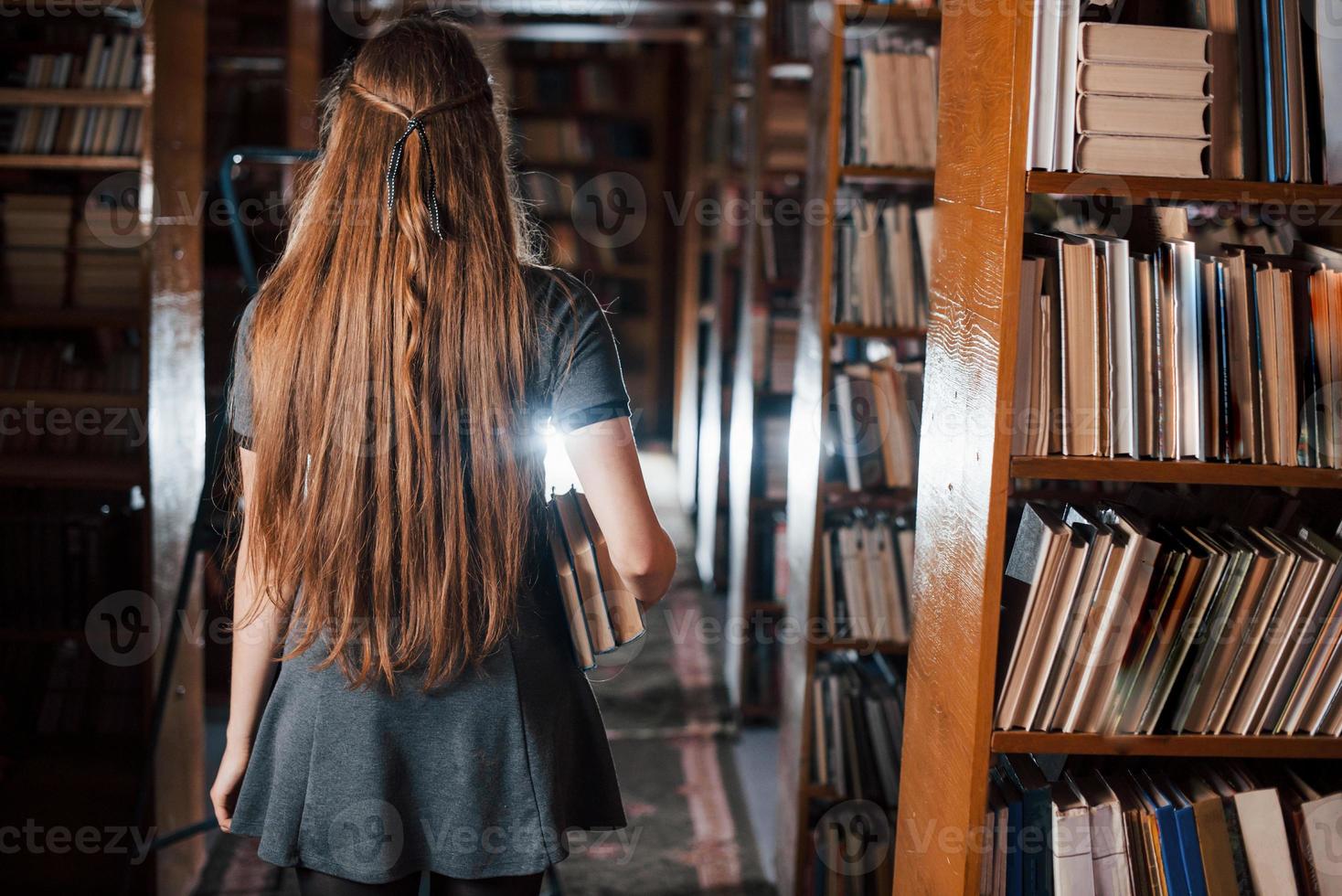 Rückansicht. Studentin ist in der Bibliothek, die voller Bücher ist. Konzeption von Bildung foto