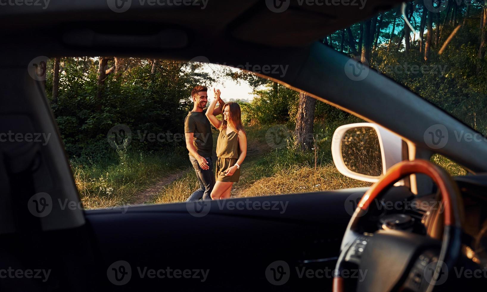 Blick aus dem Innenraum des Autos. Lenkrad, Seitenspiegel. schönes junges paar hat tagsüber eine gute zeit im wald foto
