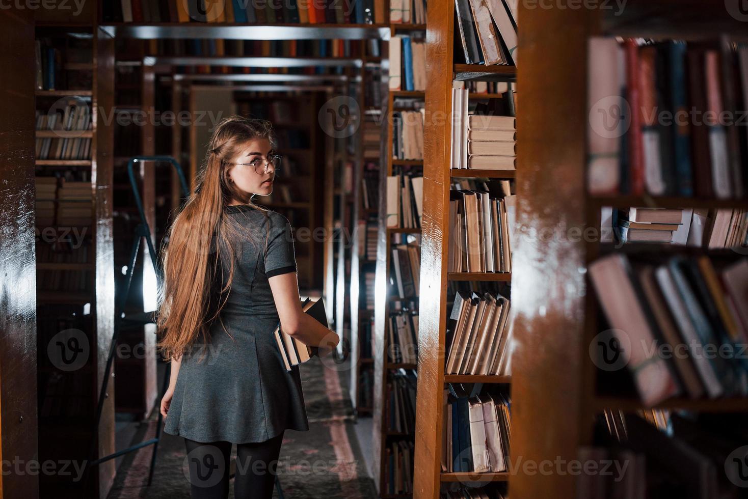 schaut hinterher. Studentin ist in der Bibliothek, die voller Bücher ist. Konzeption von Bildung foto