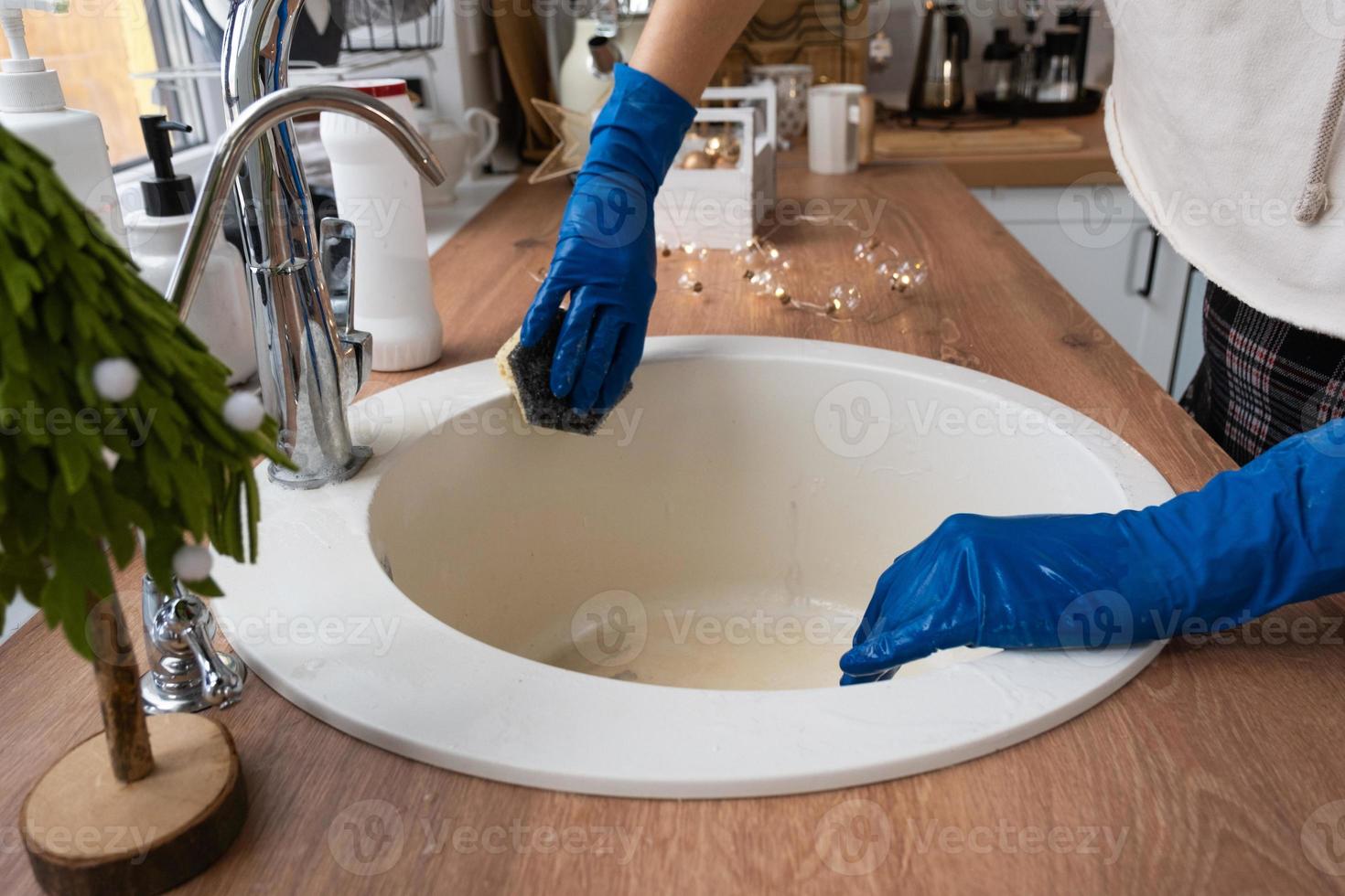 Reinigung der Spüle in der Küche vor den Weihnachts- und Neujahrsferien. Hand in Handschuhe und Schwamm, Waschmittel, Trockenpulver. festliches Dekor in der weißen Küche, gemütliches Interieur des Hauses foto