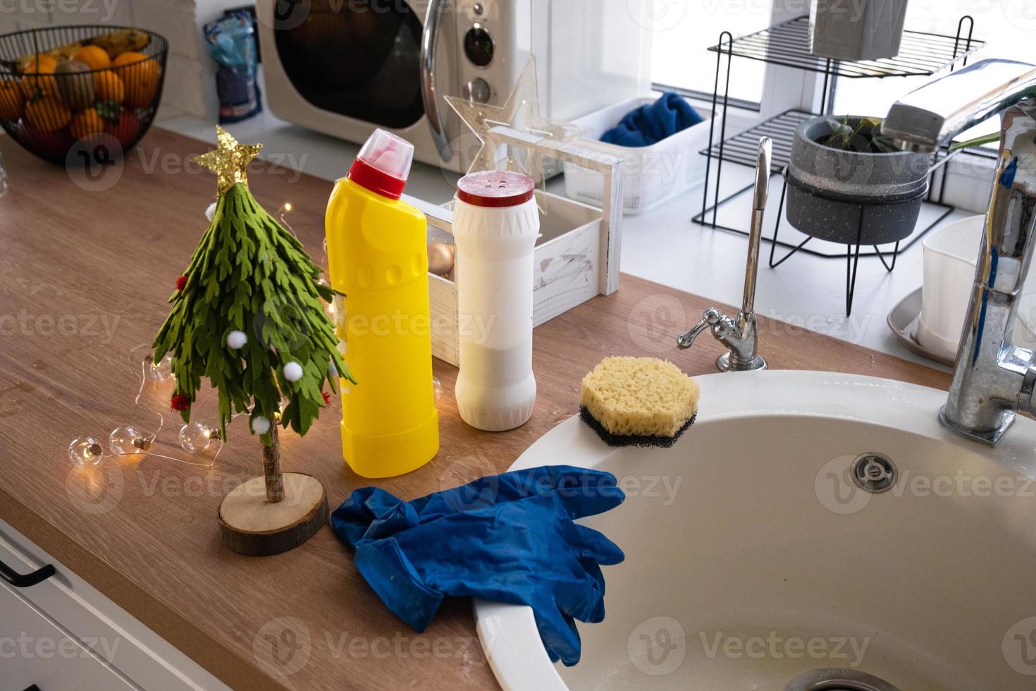 Reinigung der Küche vor den Weihnachts- und Neujahrsferien. Waschmittel, Trockenpulver, Schwamm, Handschuhe sind auf dem Waschbecken. festliches Dekor in der weißen Küche, gemütliches Interieur des Hauses foto