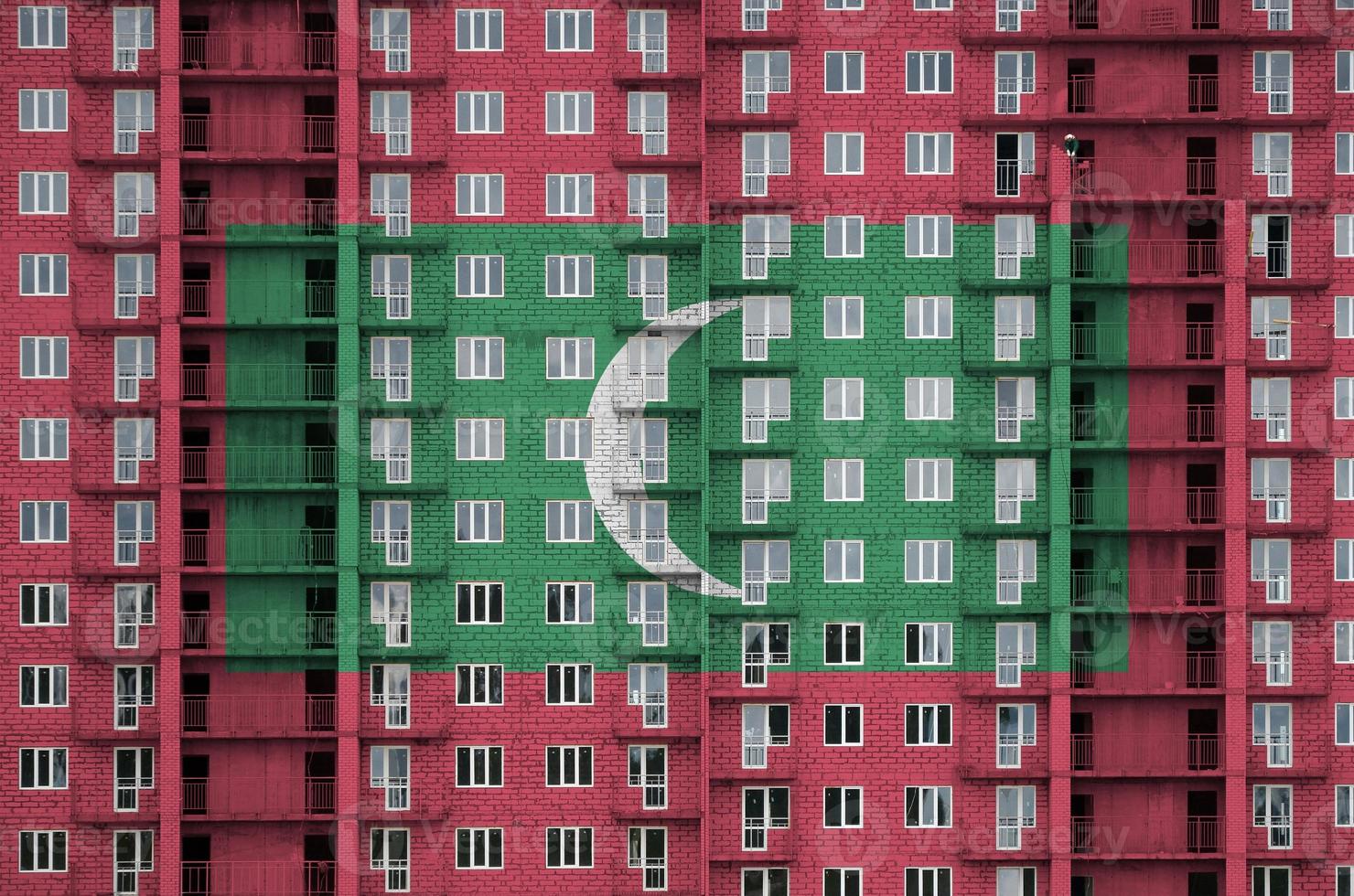 Malediven-Flagge in Lackfarben auf einem im Bau befindlichen mehrstöckigen Wohngebäude. strukturiertes banner auf backsteinmauerhintergrund foto