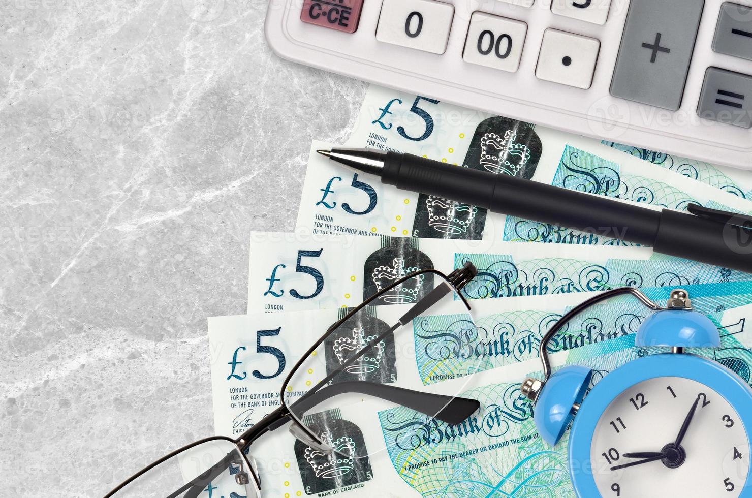 5 britische Pfund-Scheine und Taschenrechner mit Brille und Stift. Konzept für Geschäftsdarlehen oder Steuerzahlungssaison. Zeit, Steuern zu zahlen foto