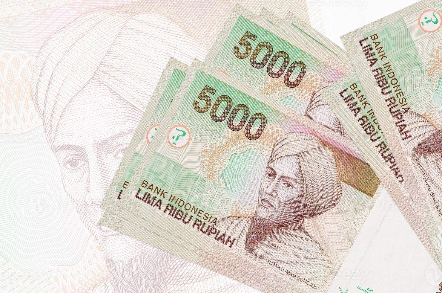 5000 indonesische Rupiah-Scheine liegen im Stapel auf dem Hintergrund einer großen halbtransparenten Banknote. abstrakte Darstellung der Landeswährung foto