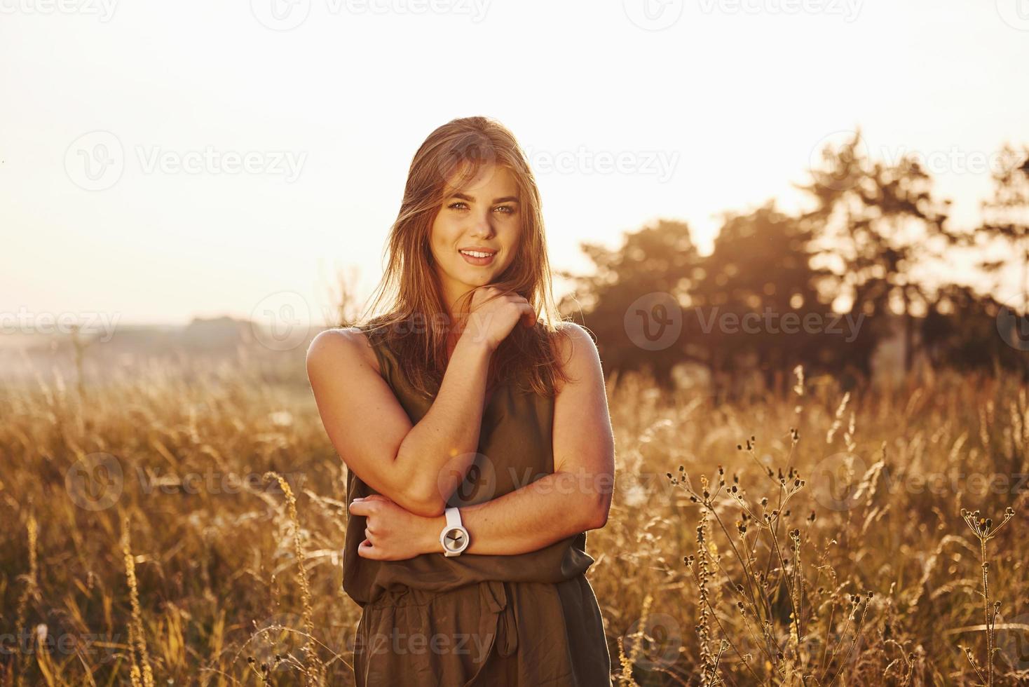 Porträt eines glücklichen Mädchens, das auf dem von Sonnenlicht beleuchteten Feld steht foto