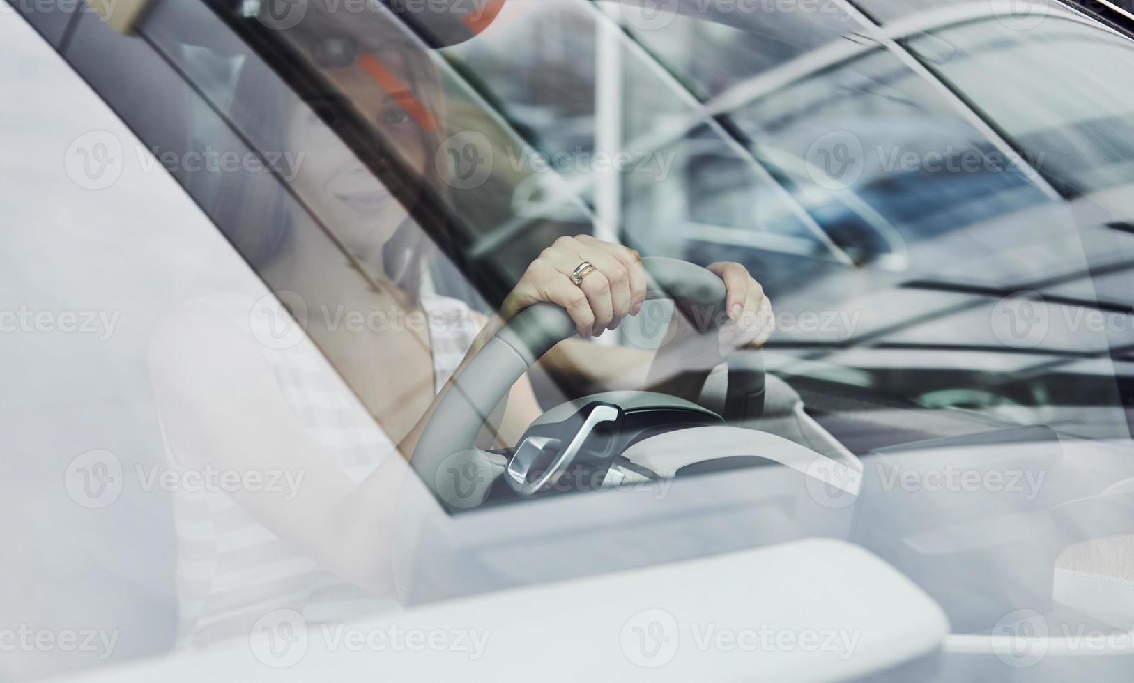 Vorderansicht. Spiegelung im Glas. Fahrerin im Inneren eines modernen Automobils. brandneues Auto testen foto