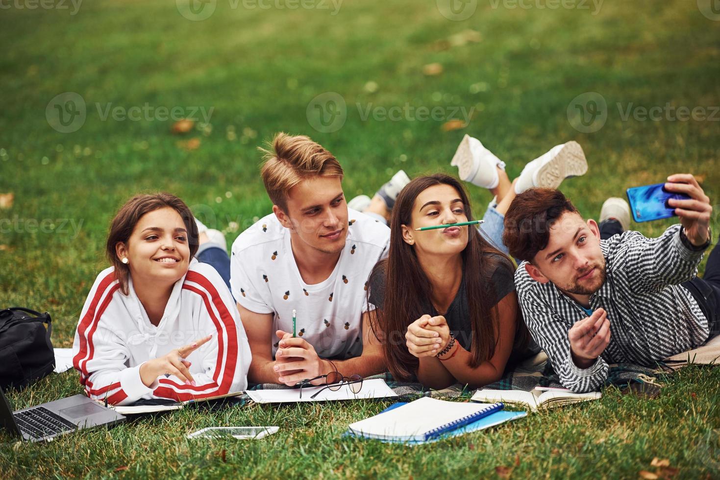 Zeit für ein Selfie. Gruppe junger Studenten in Freizeitkleidung auf grünem Gras tagsüber foto