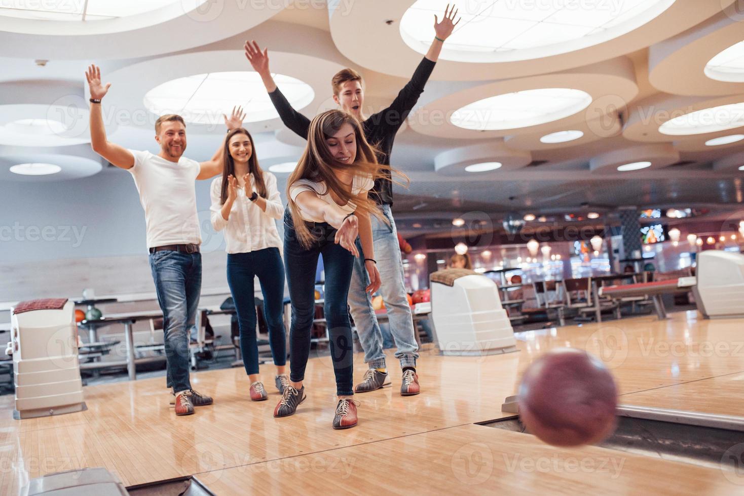 ein Mädchen unterstützen. Junge, fröhliche Freunde haben an ihren Wochenenden Spaß im Bowlingclub foto