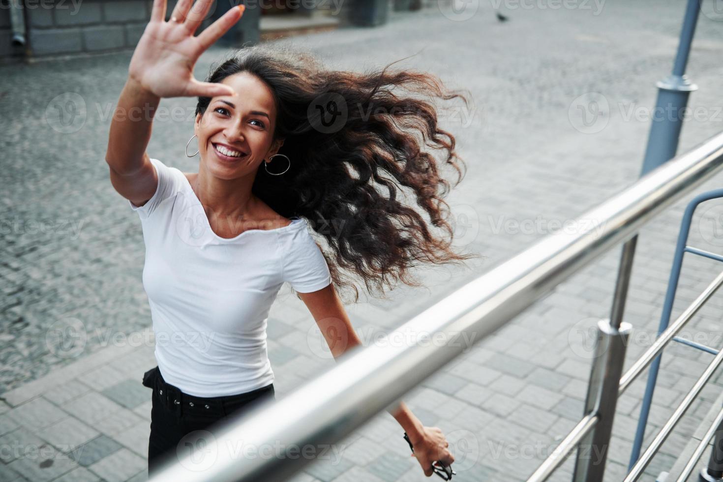 schön dich zu sehen. schöne frau mit lockigem schwarzem haar hat tagsüber eine gute zeit in der stadt foto