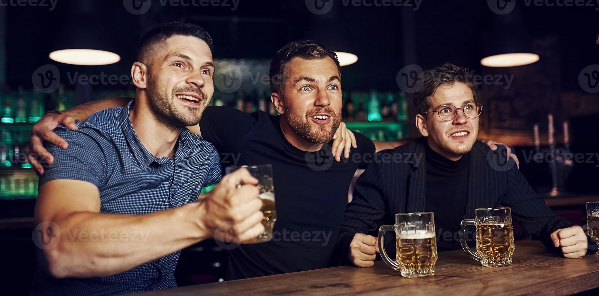 drei Sportfans in einer Bar beim Fußball schauen. mit Bier in der Hand foto