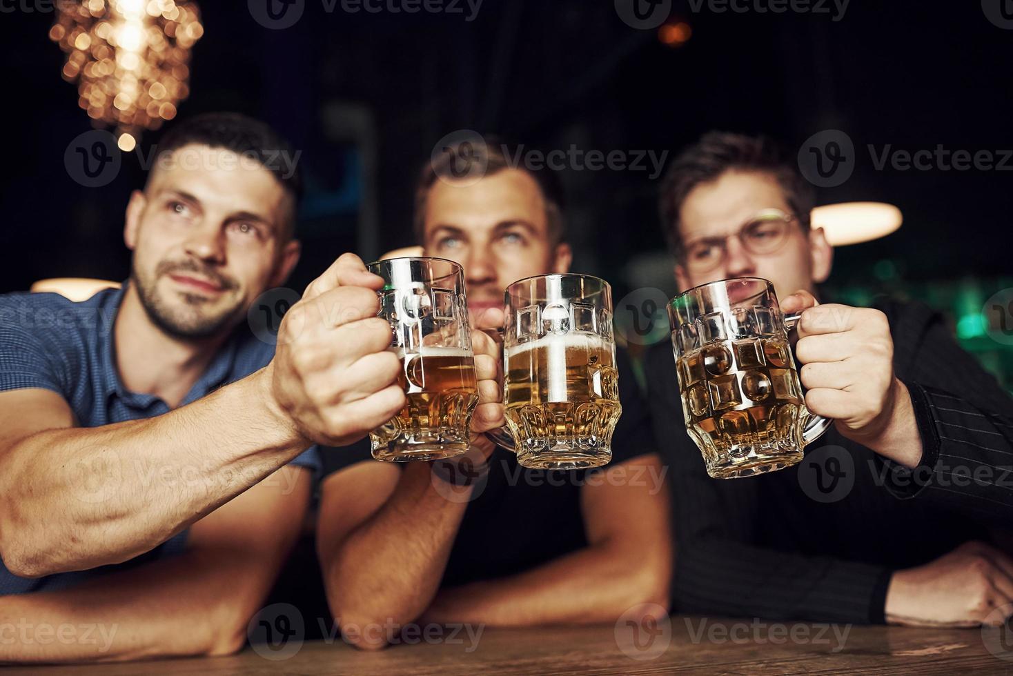 Brille klopfen. drei Sportfans in einer Bar beim Fußball schauen. mit Bier in der Hand foto