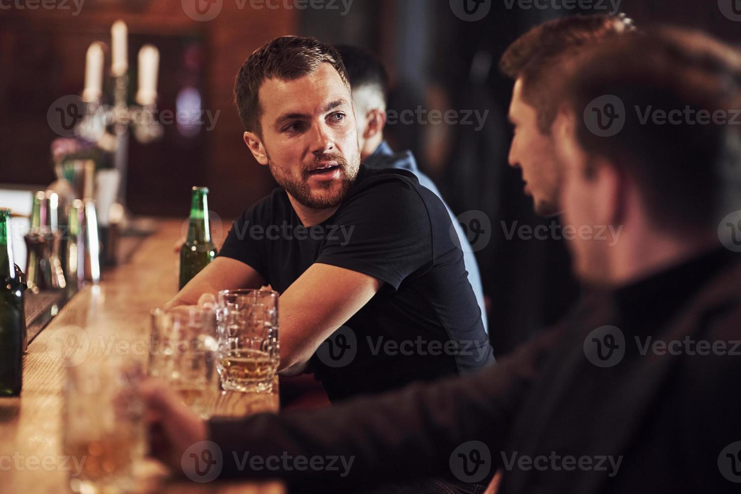 Seitenansicht. freunde ruhen sich mit bier in den händen in der kneipe aus. Gespräch haben foto