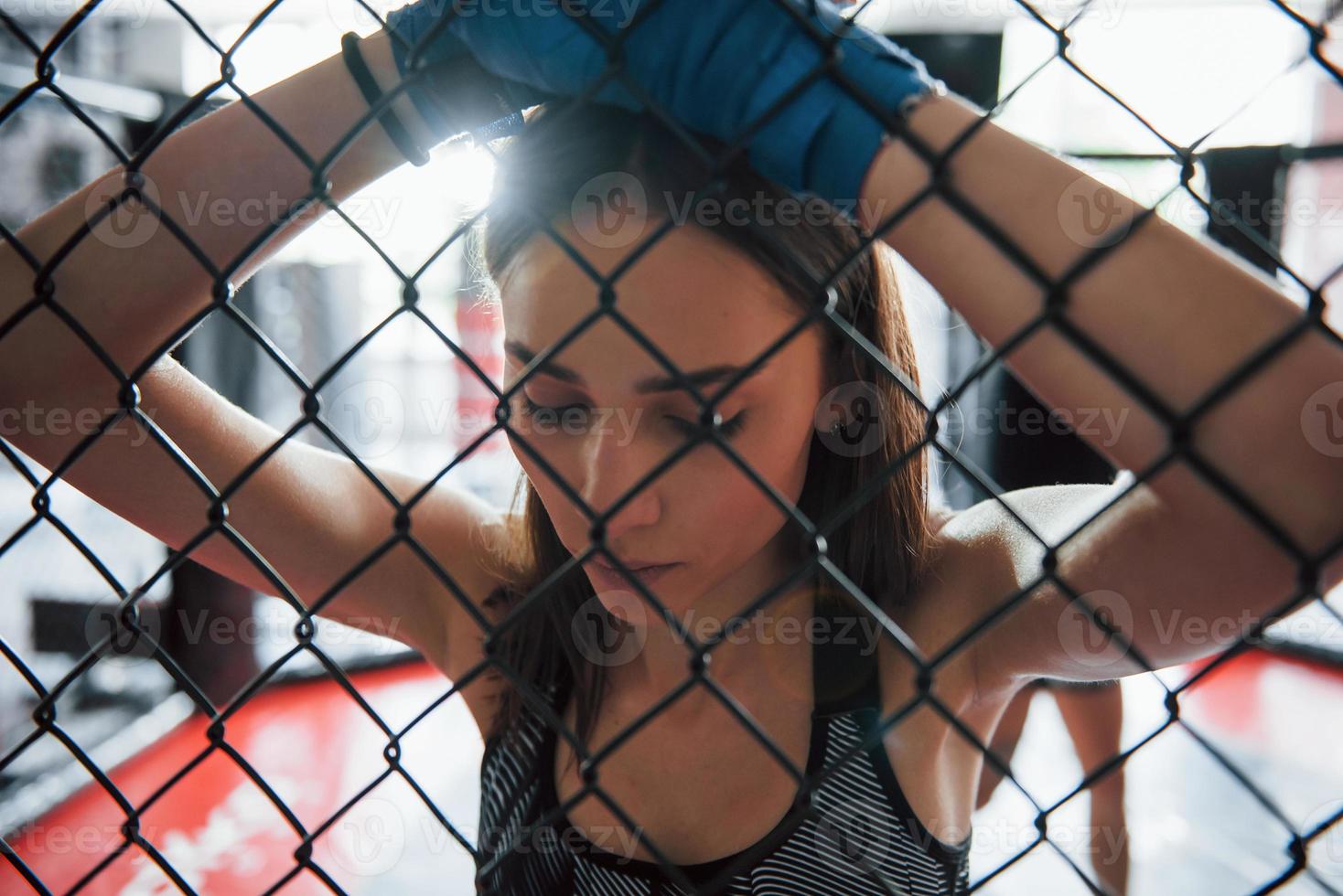 eine Pause machen. Sportlerin im Boxring hat Bewegung. an den Zaun gelehnt foto