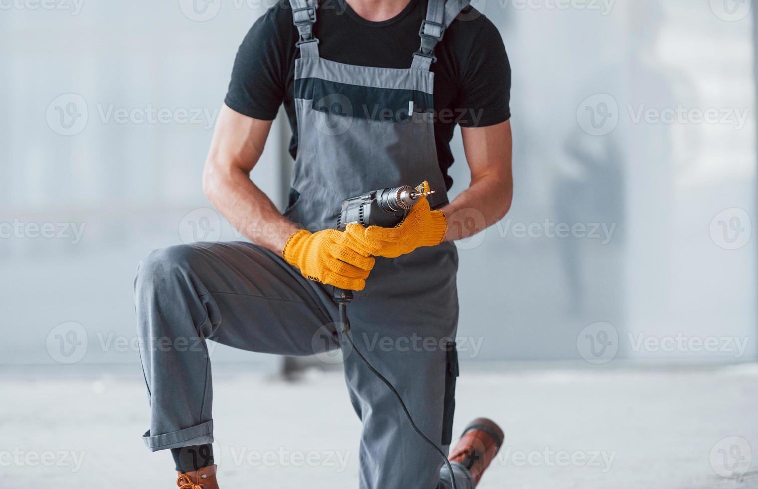 Nahaufnahme eines Mannes in grauer Uniform mit Bohrer in der Hand drinnen in einem modernen großen Büro tagsüber foto