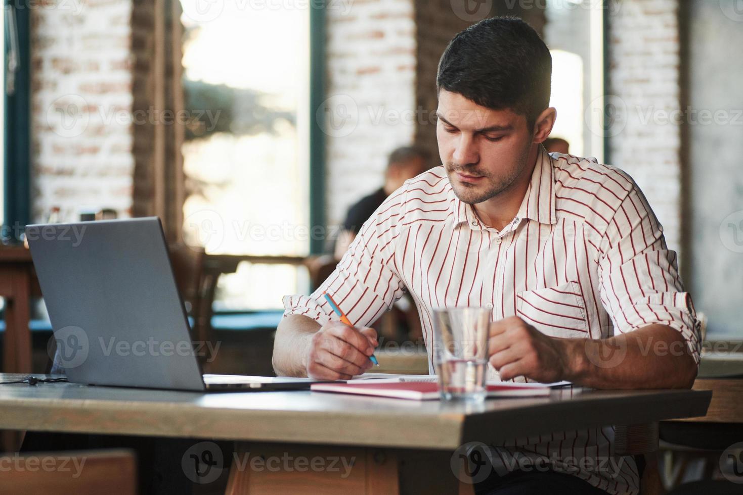 Typ, der einige Notizen in seinem Lehrbuch macht. erwachsener mann sitzt tagsüber im café und benutzt den laptop für die fernarbeit foto