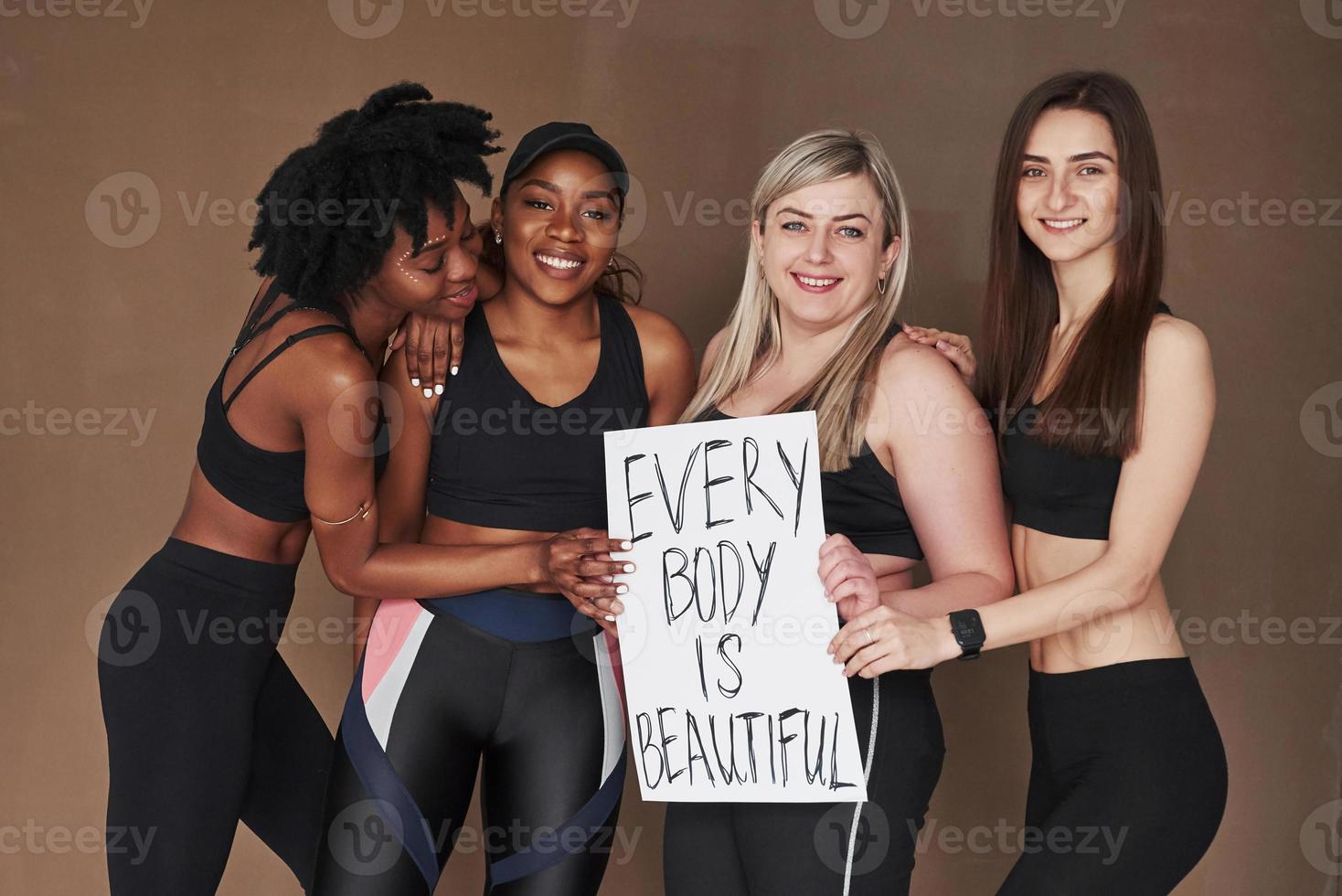 schöne Zeit haben. Gruppe multiethnischer Frauen, die im Studio vor braunem Hintergrund stehen foto