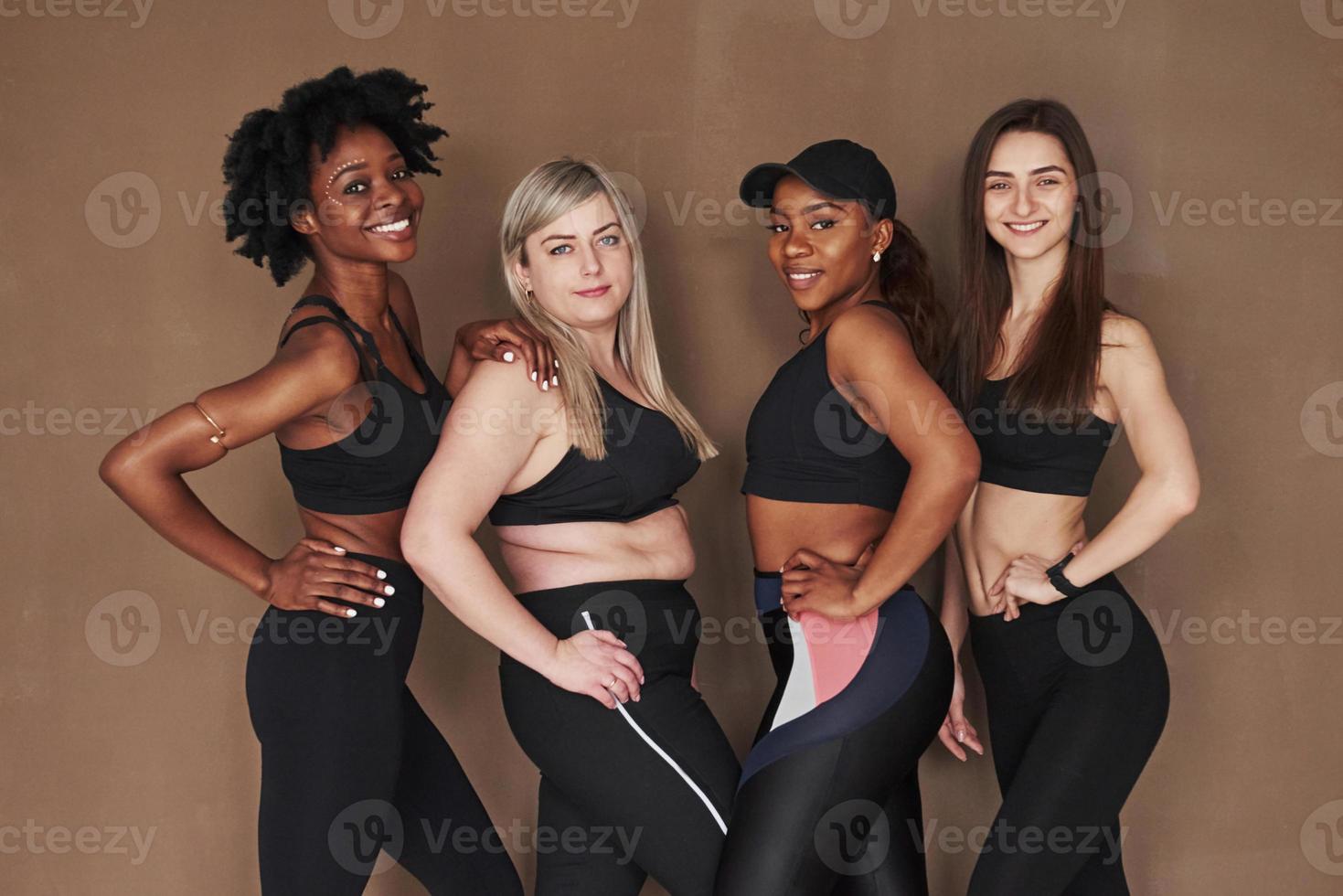 menschliche Körper. Gruppe multiethnischer Frauen, die im Studio vor braunem Hintergrund stehen foto