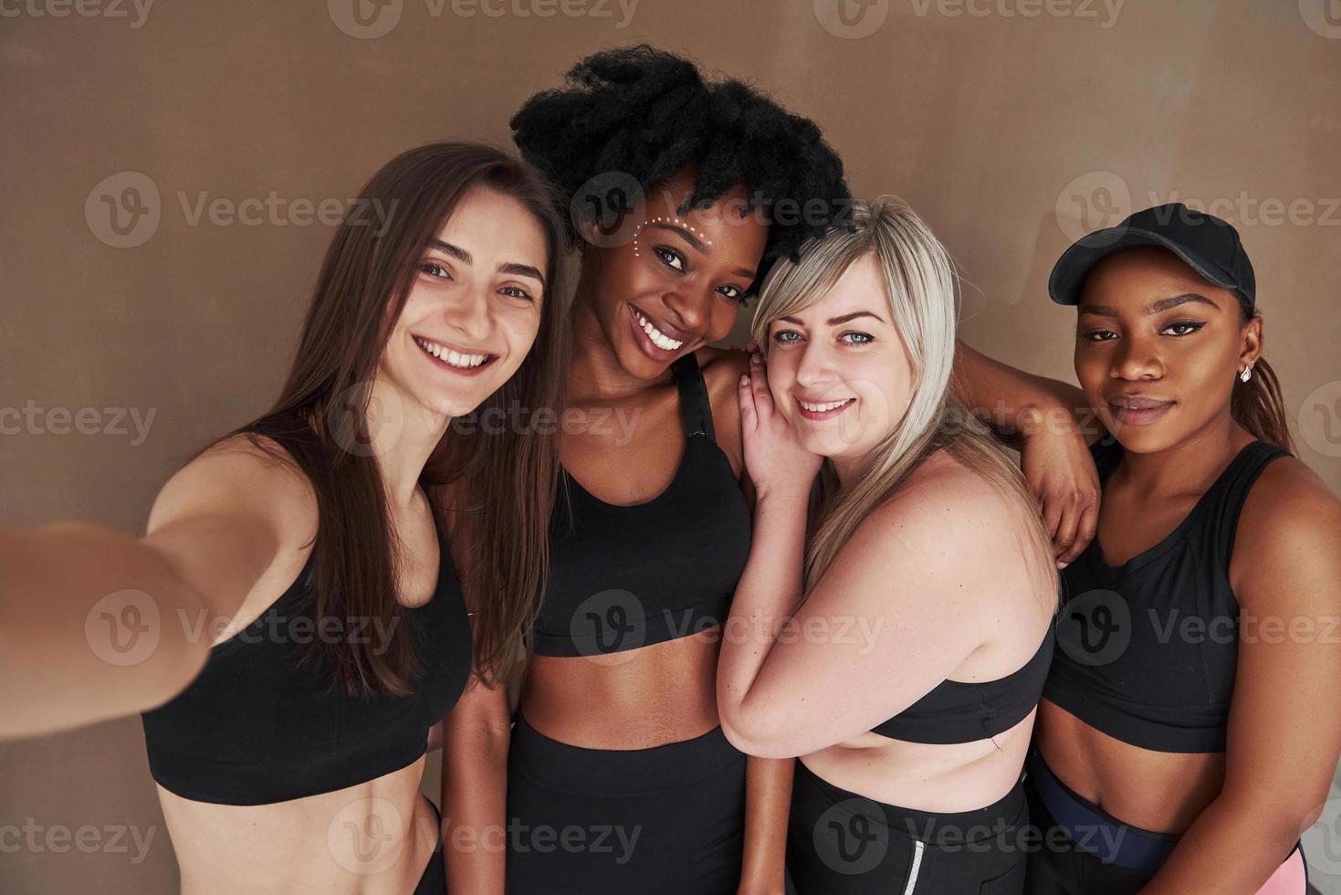 Foto wie vom Telefon. Gruppe multiethnischer Frauen, die im Studio vor braunem Hintergrund stehen