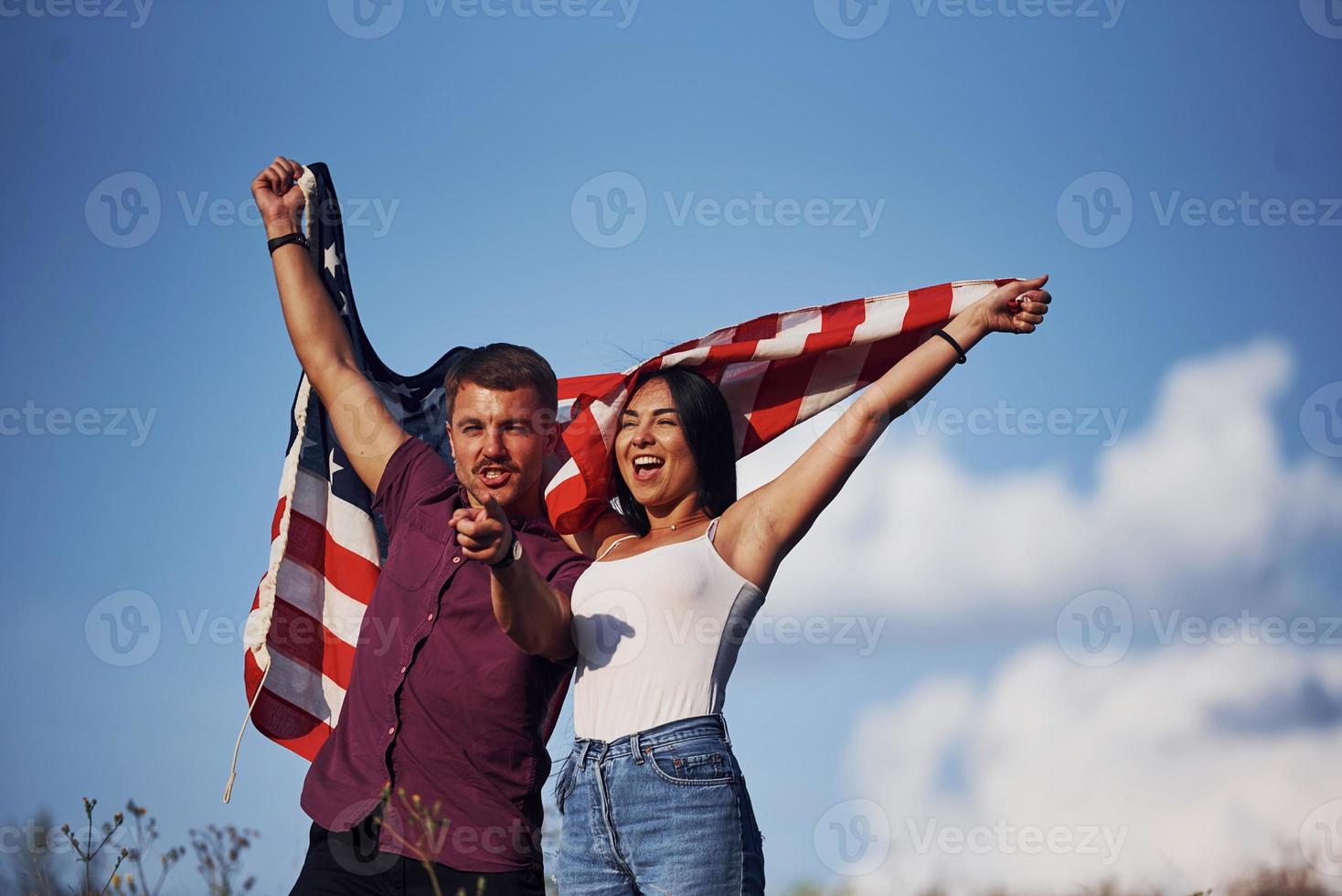 mit erhobenen Händen. fühlt Freiheit. Schönes Paar mit amerikanischer Flagge hat eine gute Zeit im Freien auf dem Feld foto