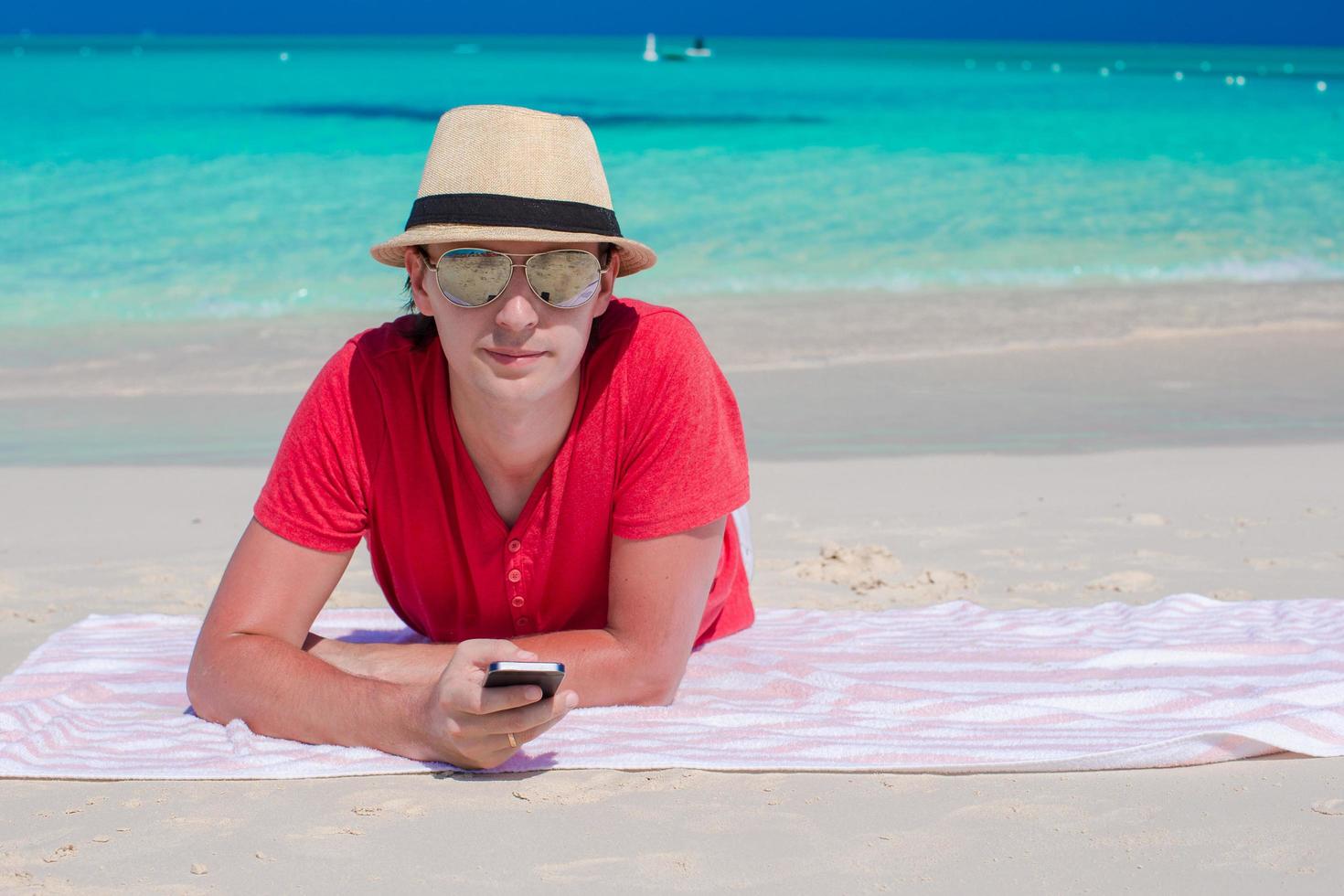 Mann, der mit seinem Telefon am Strand liegt foto