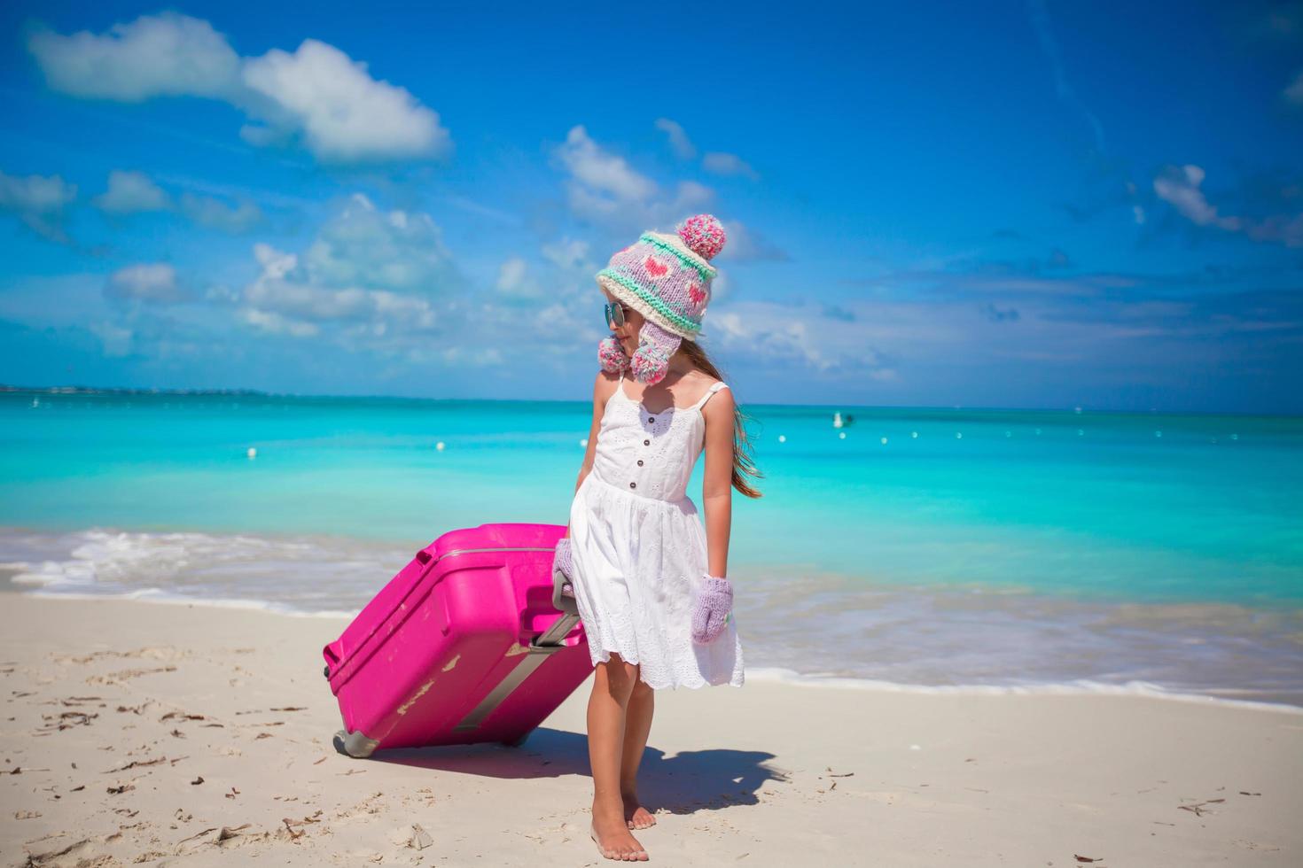 Mädchen in Wintermütze und Fäustlinge, die mit Gepäck auf einem Strand gehen foto