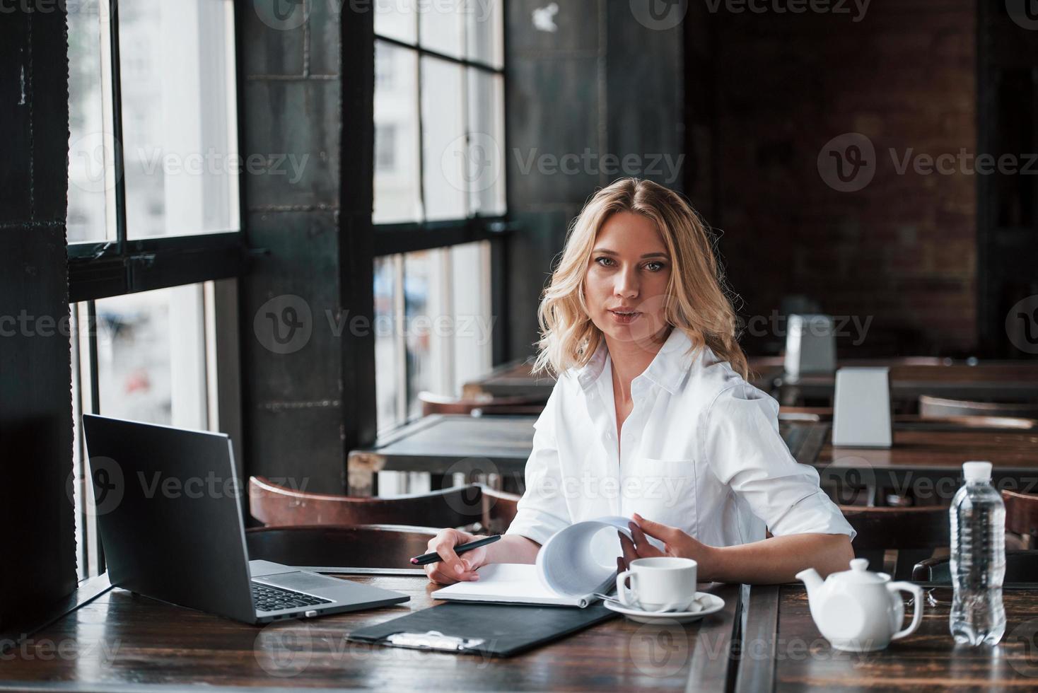 muss einige Informationen in meinem Notizblock finden. Geschäftsfrau mit lockigen blonden Haaren drinnen im Café tagsüber foto