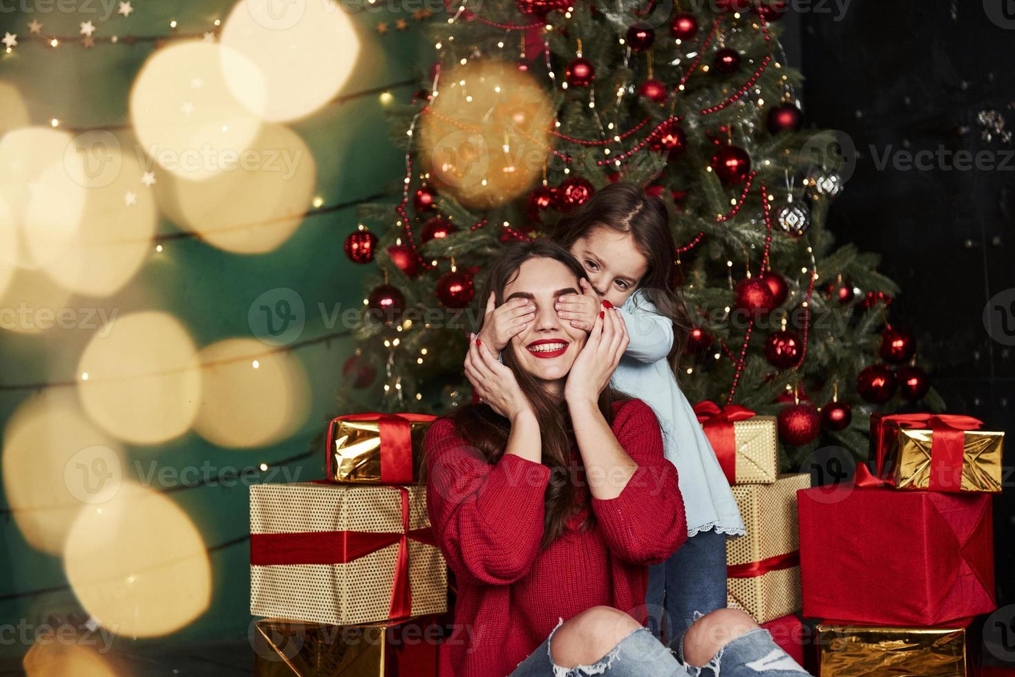 gute Familienzeit verbringen. süßes kleines Mädchen, das die Augen ihrer Mutter bedeckt. schönes zimmer mit weihnachtsbaum und weihnachtsdekoration foto