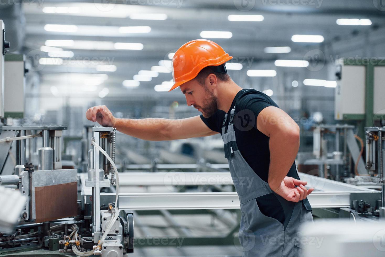 Bediener der Maschine. Industriearbeiter drinnen in der Fabrik. junger Techniker mit orangefarbenem Schutzhelm foto