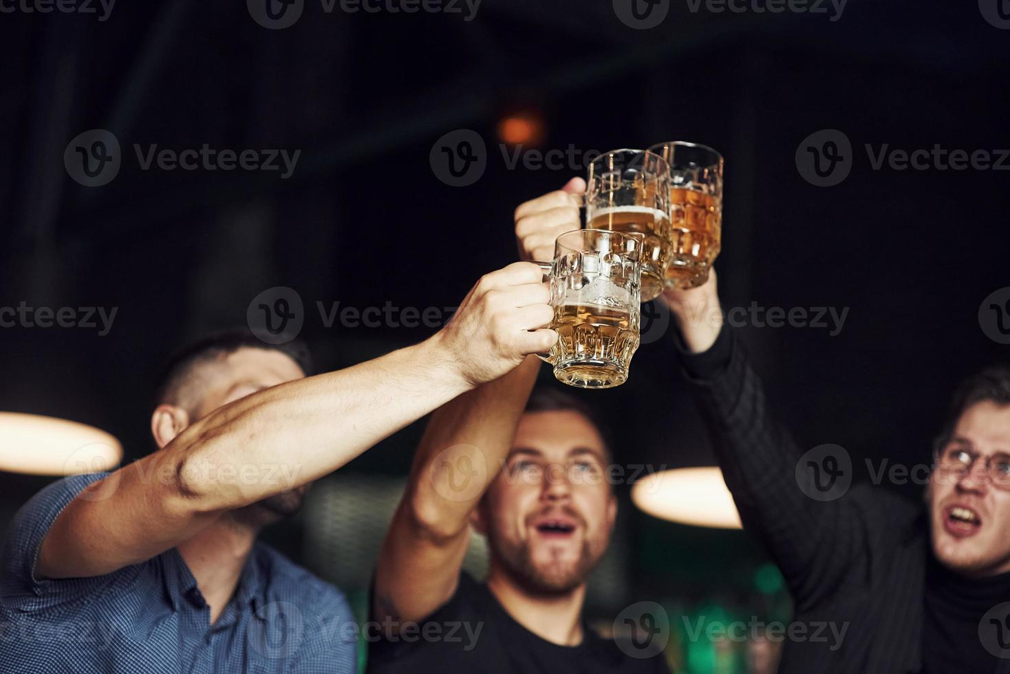 Brille klopfen. drei Sportfans in einer Bar beim Fußball schauen. mit Bier in der Hand foto