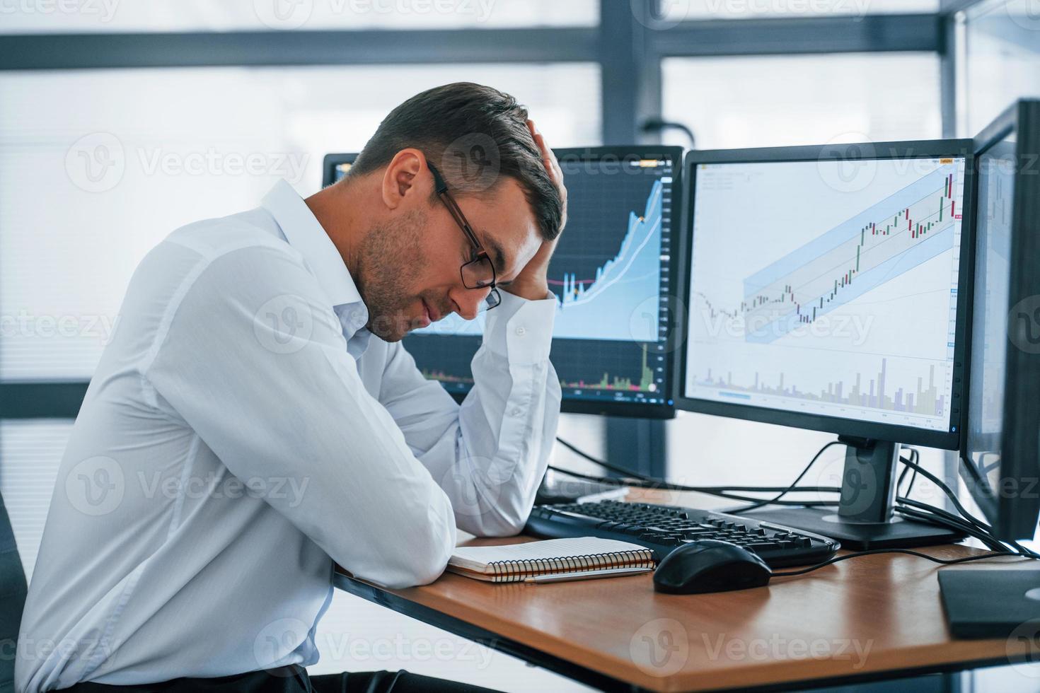 arbeitet mit Dokumenten. Der junge Geschäftsmann in formeller Kleidung ist mit mehreren Bildschirmen im Büro. Begriff von Tausch und Geld foto