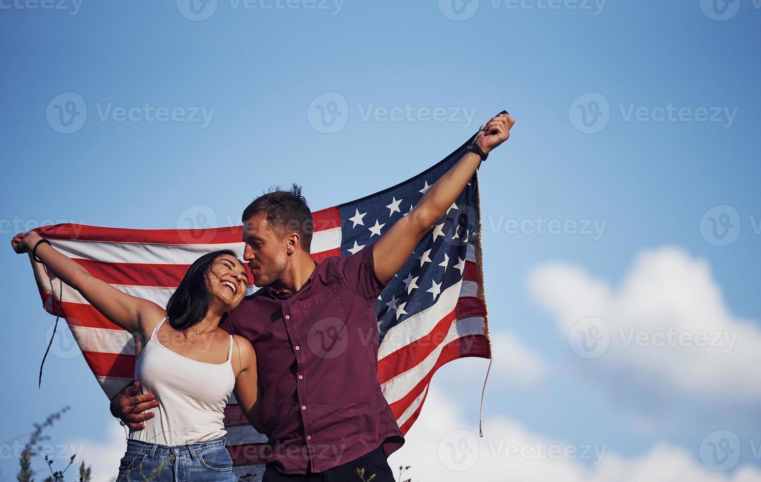 fühlt Freiheit. Schönes Paar mit amerikanischer Flagge hat eine gute Zeit im Freien auf dem Feld foto