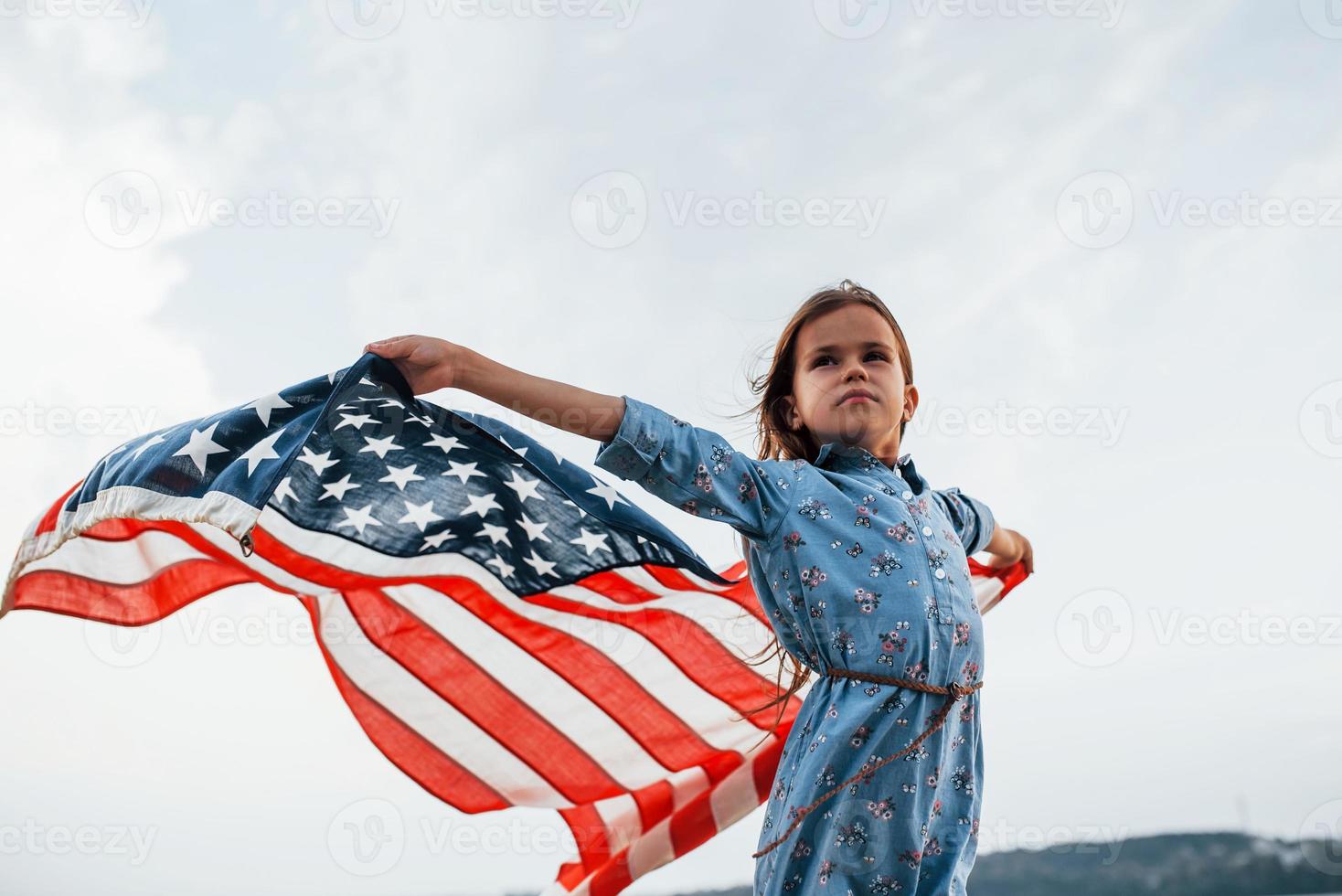 patriotisches weibliches kind mit amerikanischer flagge in den händen. gegen bewölkten Himmel foto