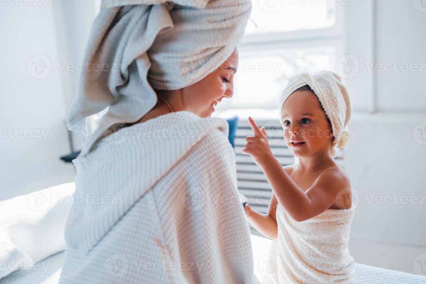 Verwendung von Creme zur Reinigung der Haut. junge mutter mit ihrer tochter haben einen schönheitstag drinnen im weißen raum foto