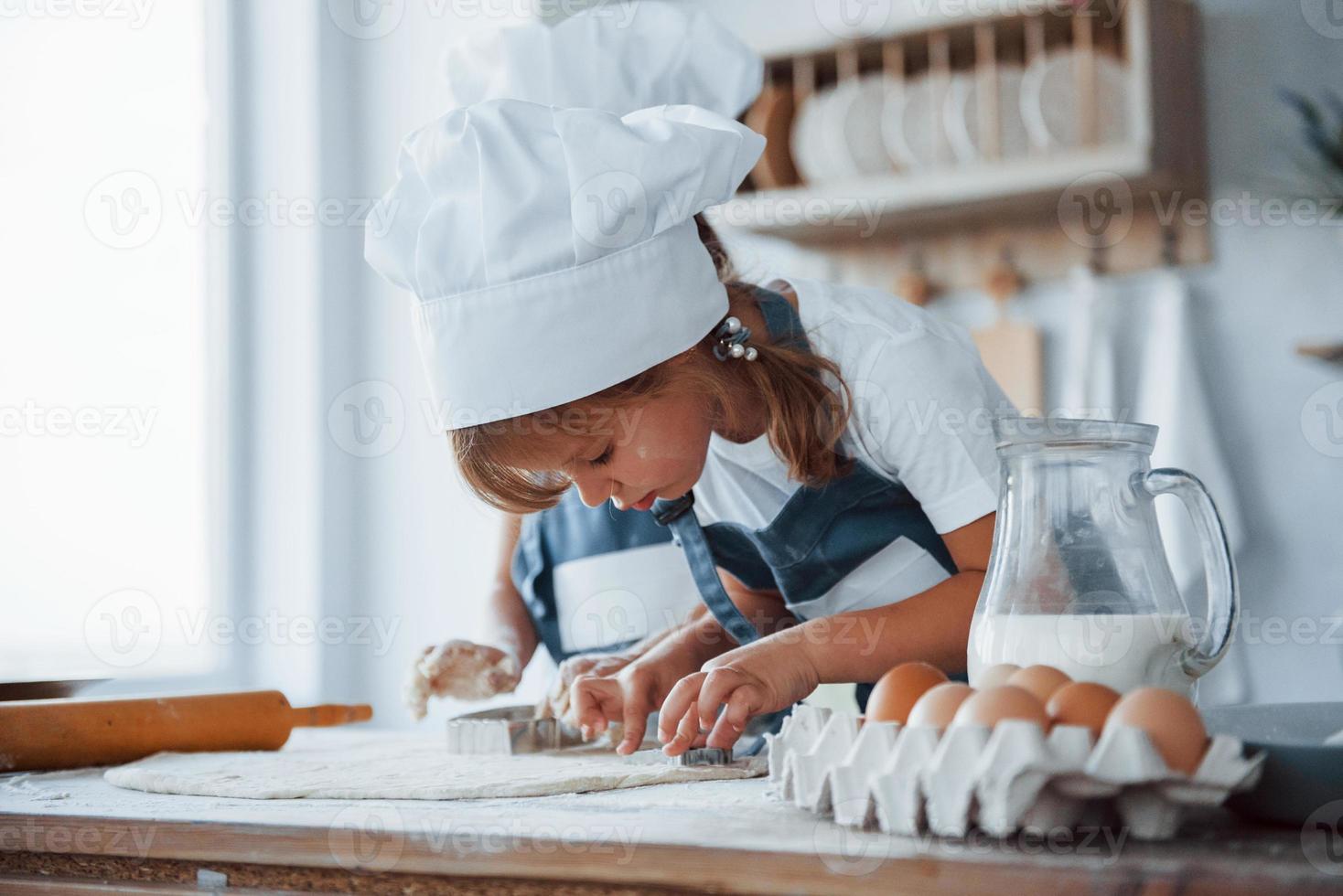 Konzentration aufs Kochen. Familienkinder in weißer Kochuniform bereiten Essen in der Küche zu foto